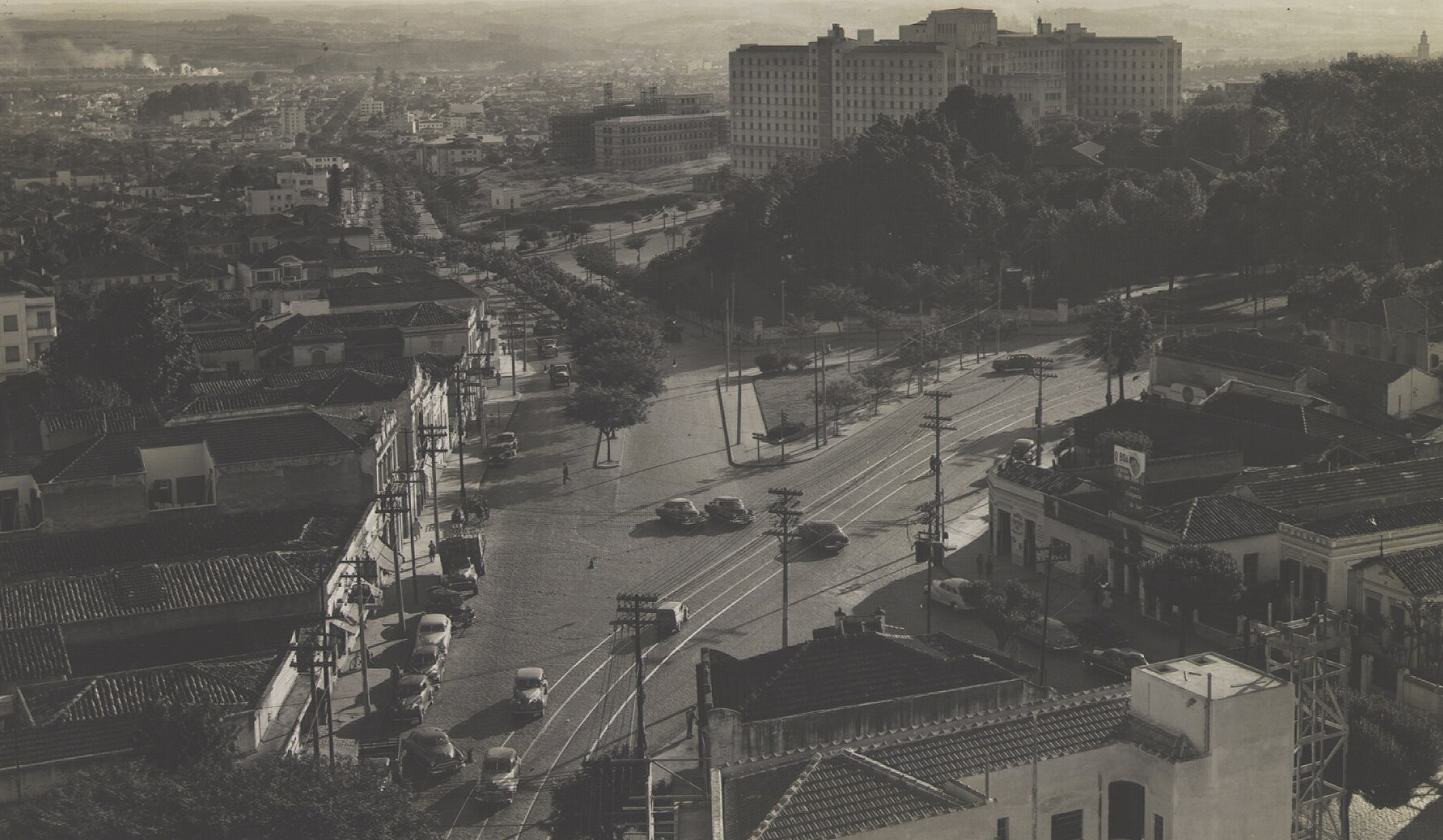 Black and white archive photograph of a wide São Paulo avenue with tram lines and parked cars, with the large Hospital das Clínicas building in the distance