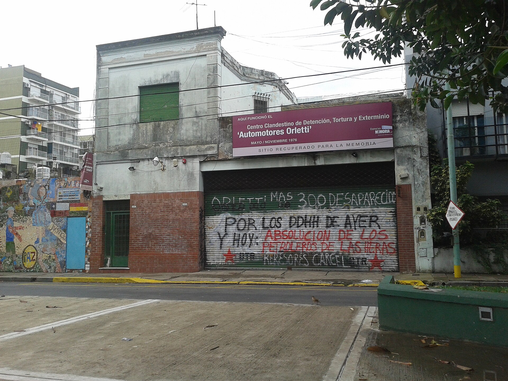 The former Automotores Orletti building in Buenos Aires with a memorial sign above a shuttered garage door covered in graffiti