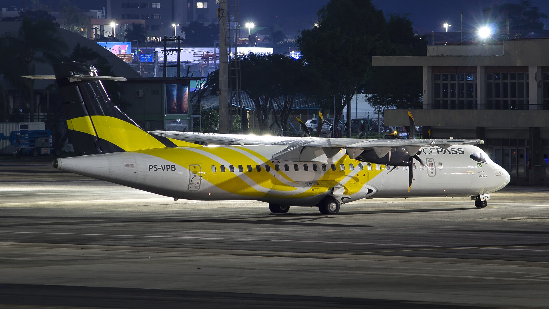 A white ATR 72-500 turboprop with yellow tail livery and VOEPASS titles, registration PS-VPB, parked on an airport apron at night