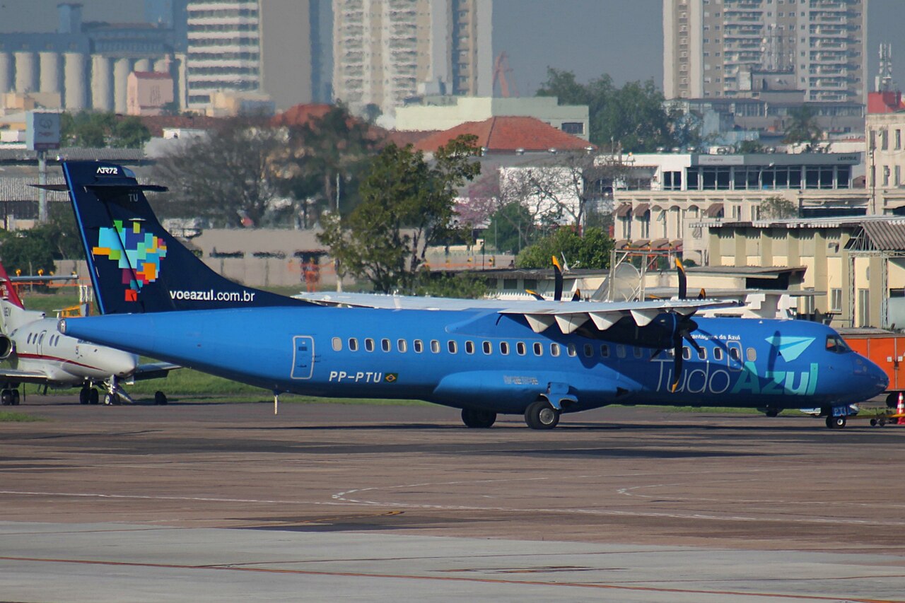 A blue Azul ATR 72-500 turboprop with PP-PTU on the fuselage parked on an airport apron with city buildings behind