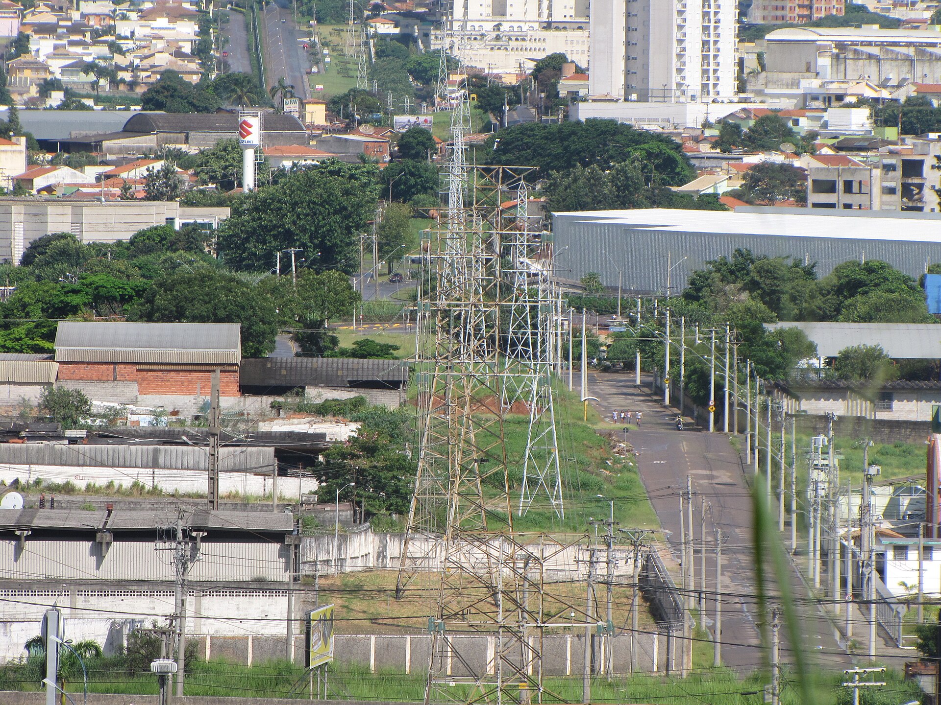 Steel high-voltage transmission towers rise above houses, trees and apartment blocks in a Brazilian city