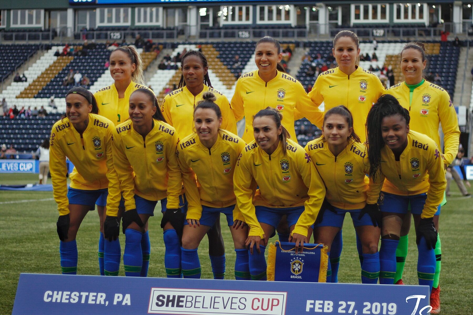 Eleven Brazil women's national team players in yellow jerseys posing for a team photo on the pitch at a SheBelieves Cup match in Chester, Pennsylvania