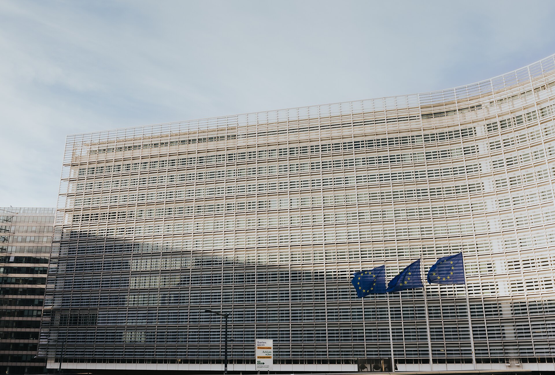 The curved glass and white louvre facade of the Berlaymont building in Brussels with three EU flags in front