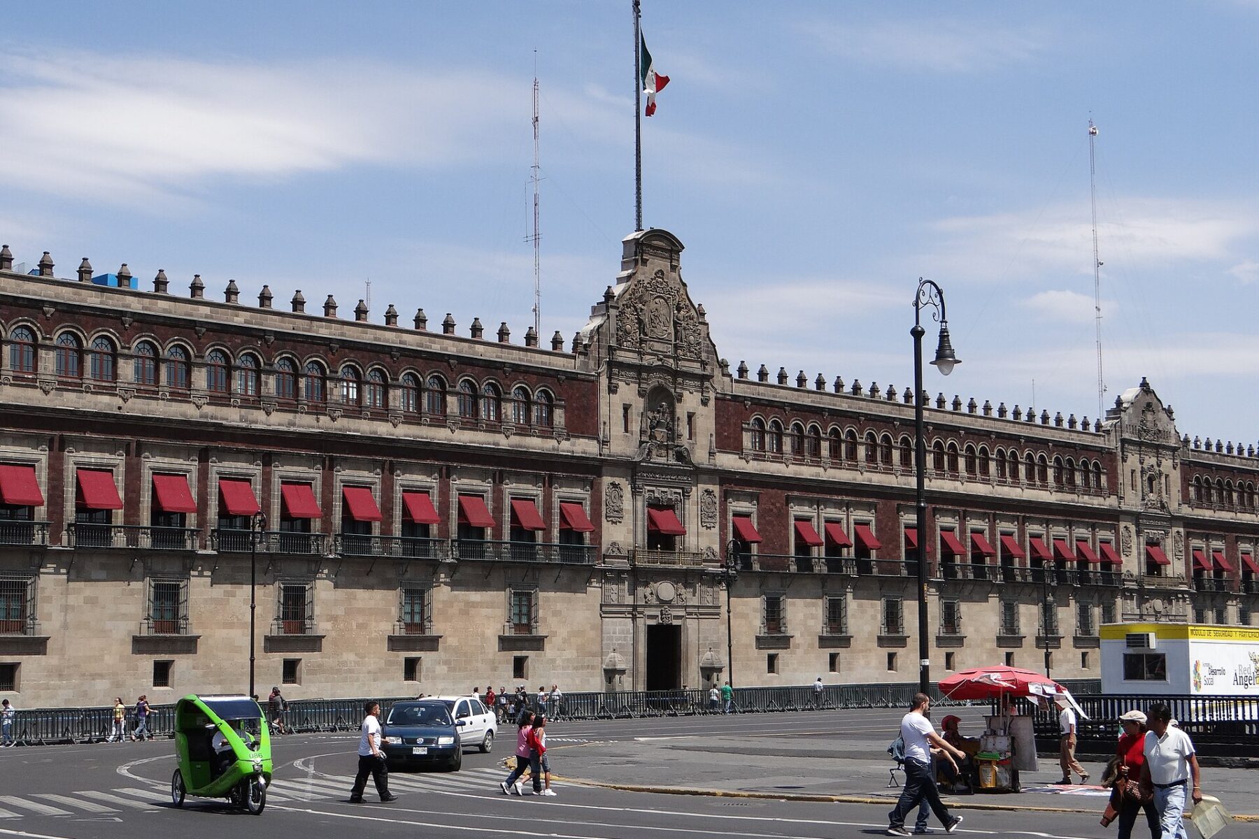The long stone and red facade of the National Palace in Mexico City, seen from the Zocalo square, with the Mexican flag flying above