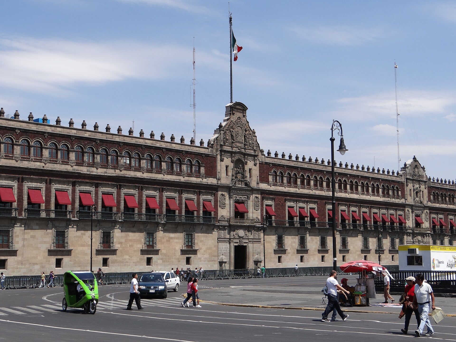 The long stone and red facade of the National Palace in Mexico City, seen from the Zocalo square, with the Mexican flag flying above