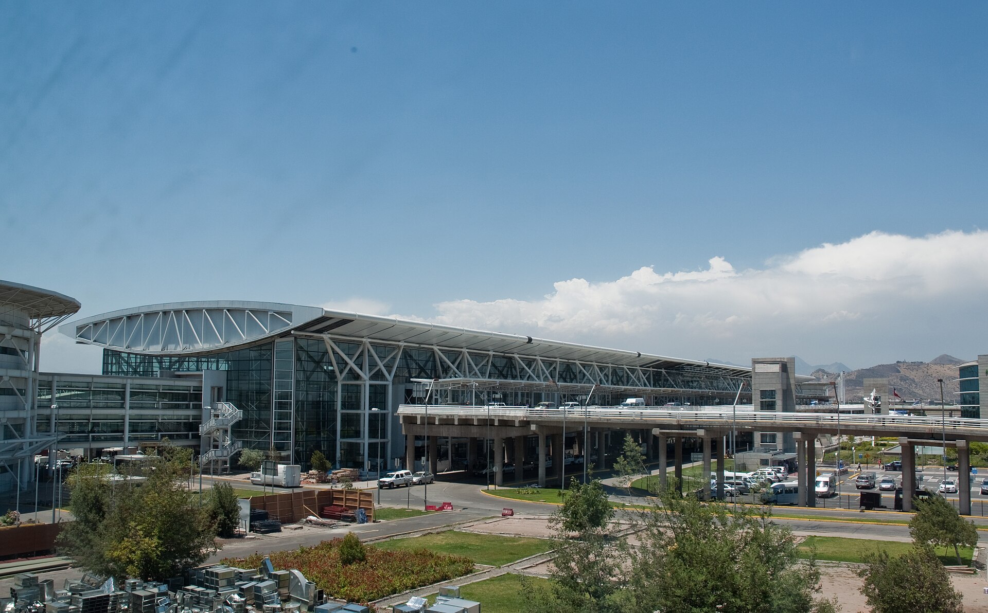 The glass and steel terminal building of Santiago's international airport under a blue sky with mountains behind