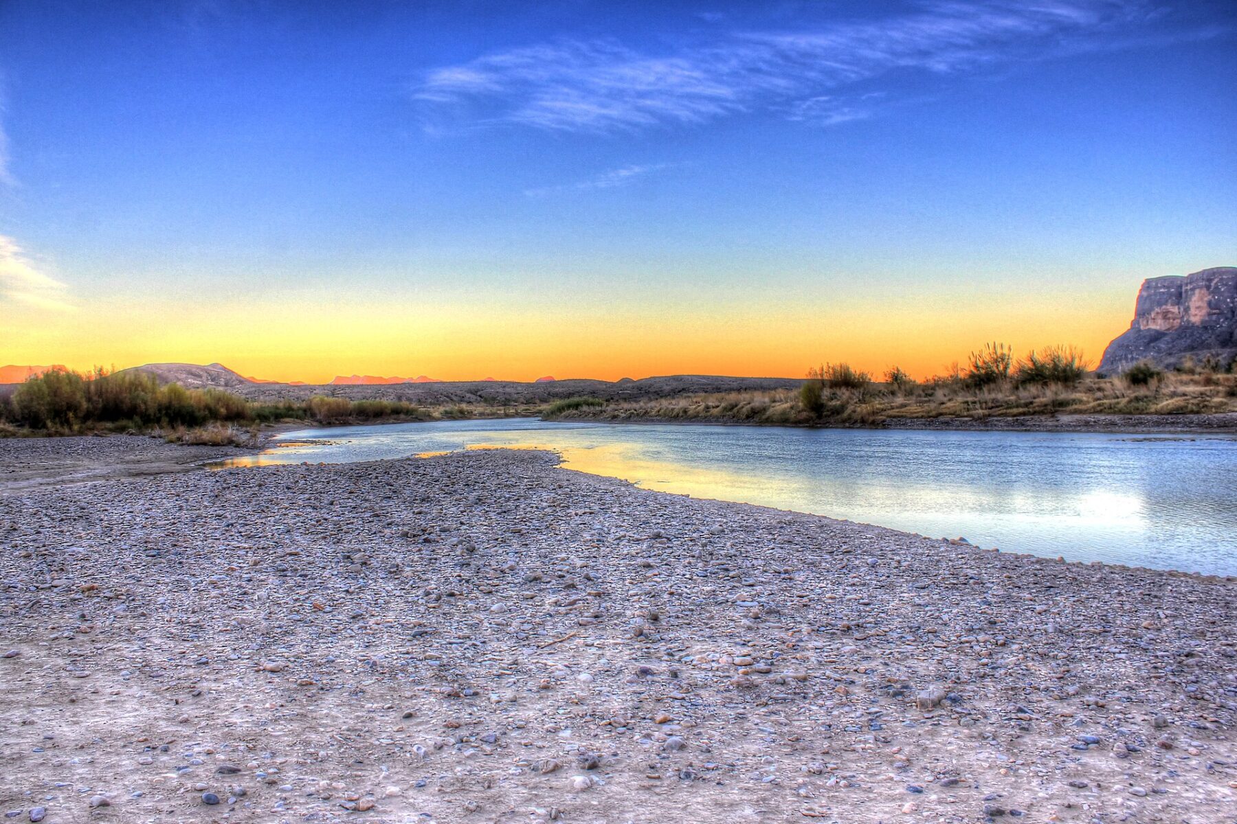 The Rio Grande at dusk in Big Bend National Park, Texas, with a gravel bank in front and a sandstone bluff on the right