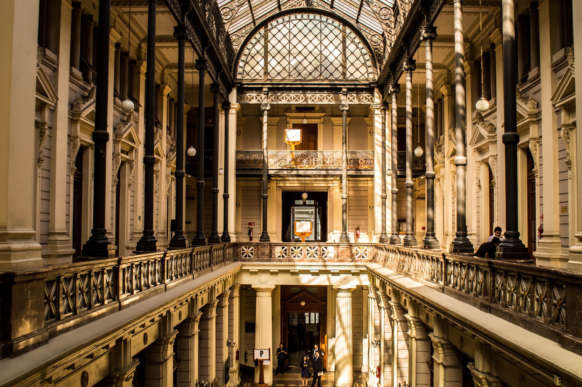 A grand interior hall of the Supreme Court building in Santiago with iron columns, balustrades, a glass roof and a few people below