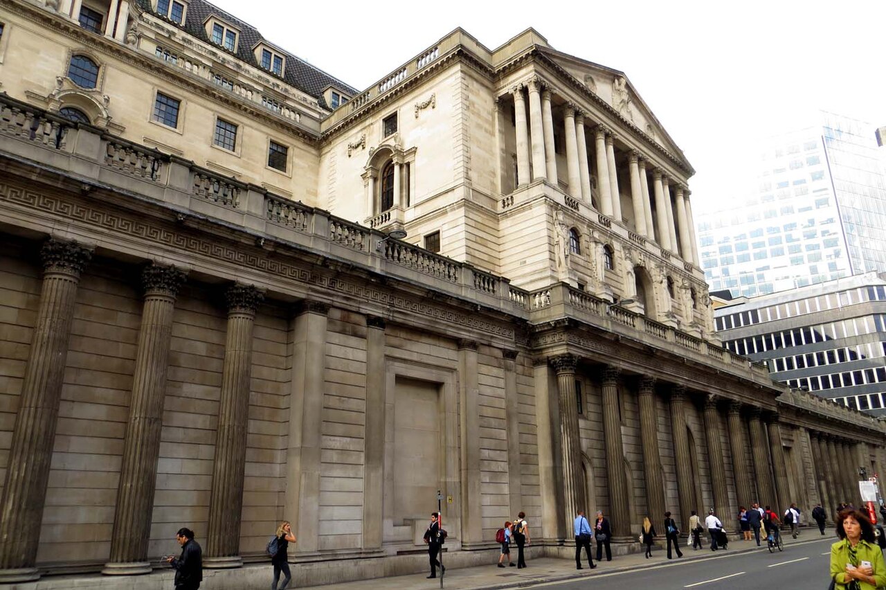 The columned stone facade of the Bank of England on Threadneedle Street in London, with pedestrians passing along the pavement