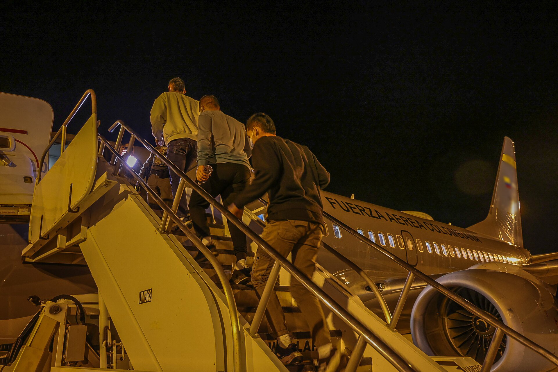 Men in casual clothes climb airstair steps at night to board a Colombian Air Force passenger jet