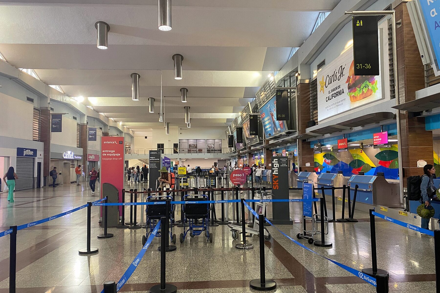 The departures hall at Las Americas International Airport near Santo Domingo, with check-in counters on the right and blue queue barriers in the foreground