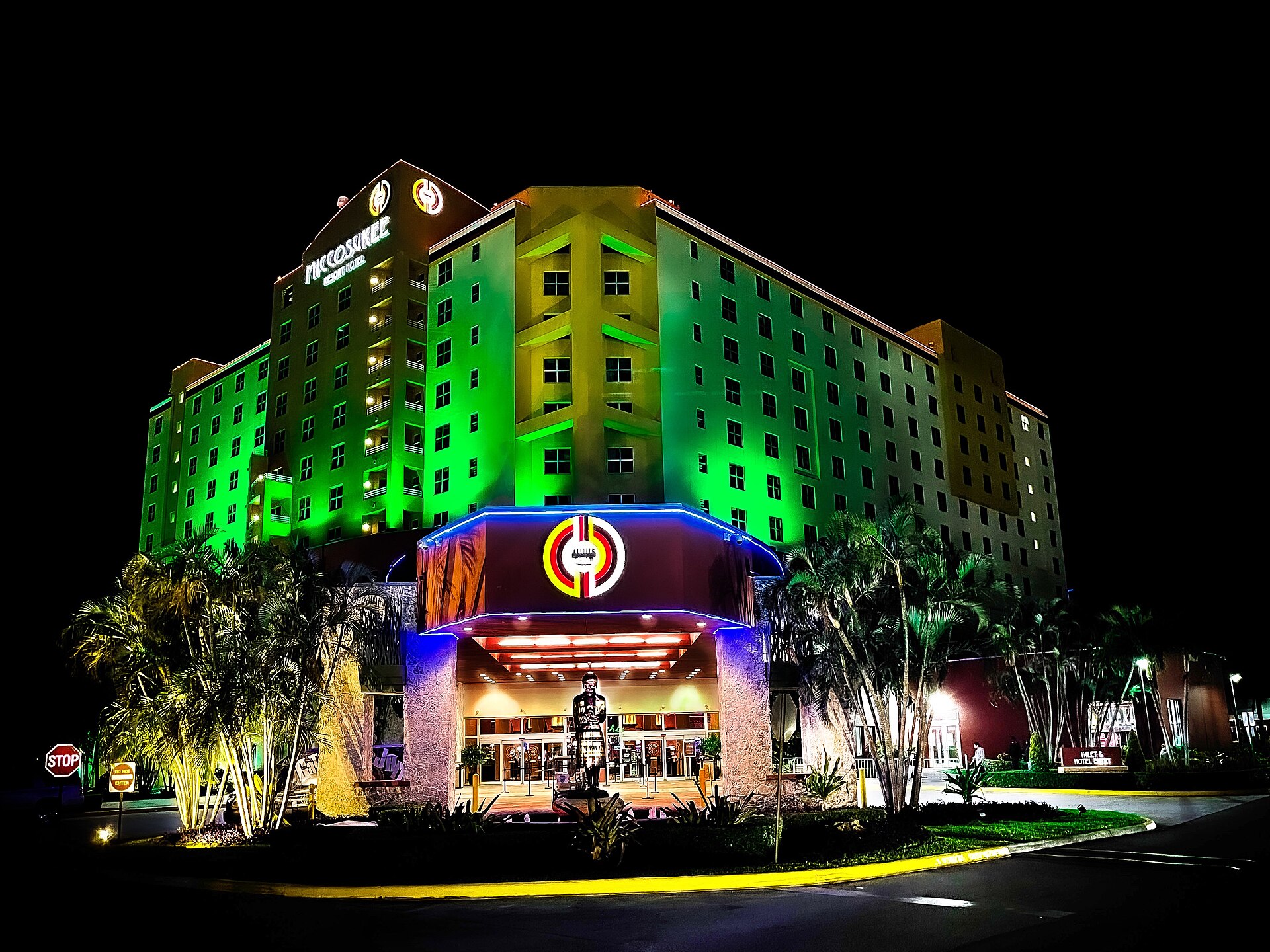 A lit hotel tower and casino entrance at night, green floodlit facade with the Miccosukee name