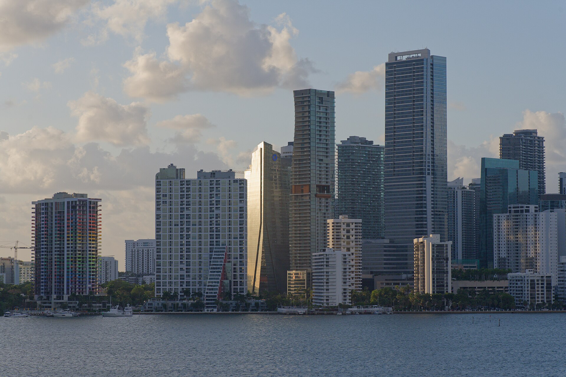 Glass and concrete towers of downtown Miami rising above Biscayne Bay under a partly cloudy sky