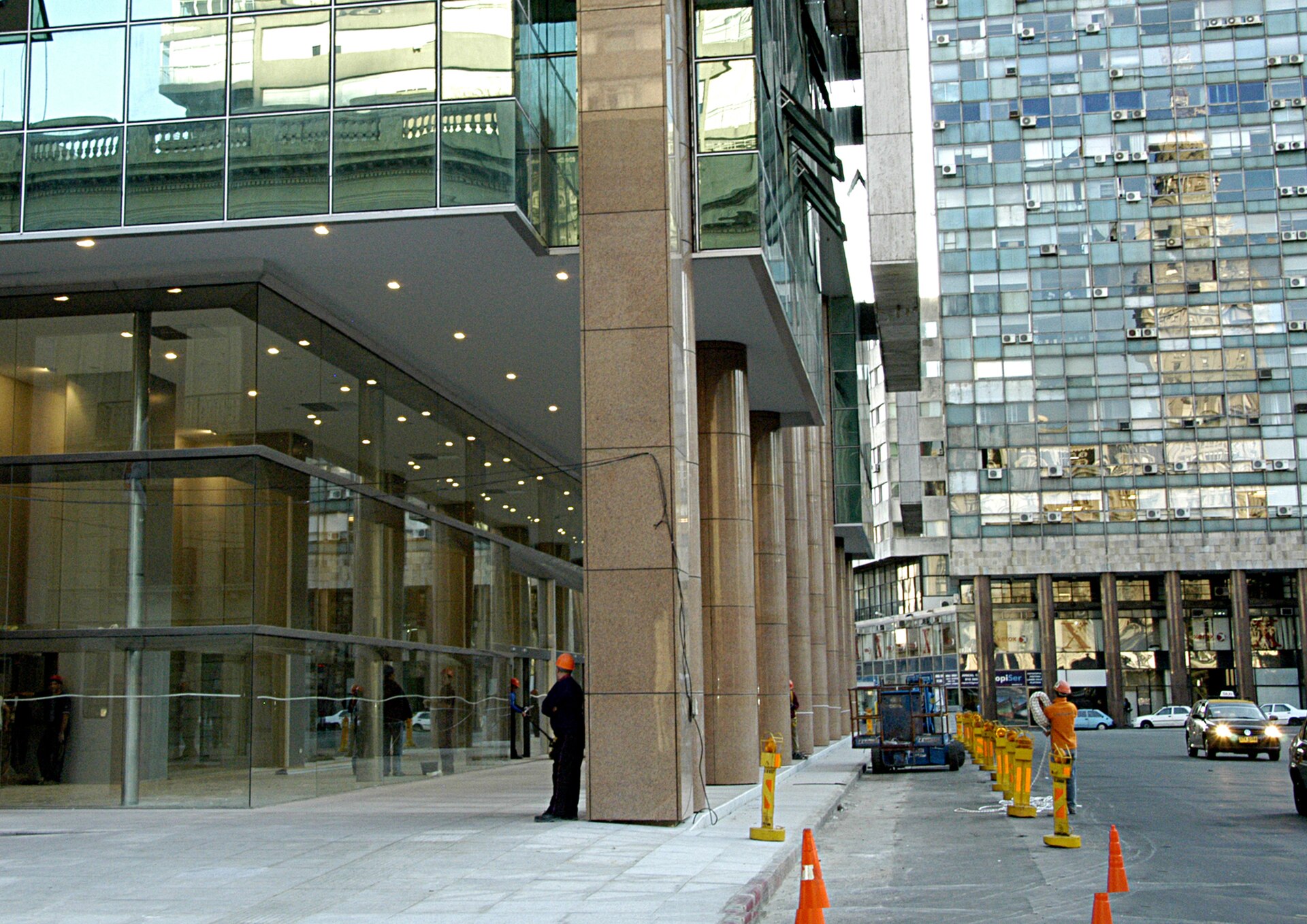 Glass-fronted base of the Torre Ejecutiva in Montevideo with stone columns, workers in hard hats and traffic cones on the street