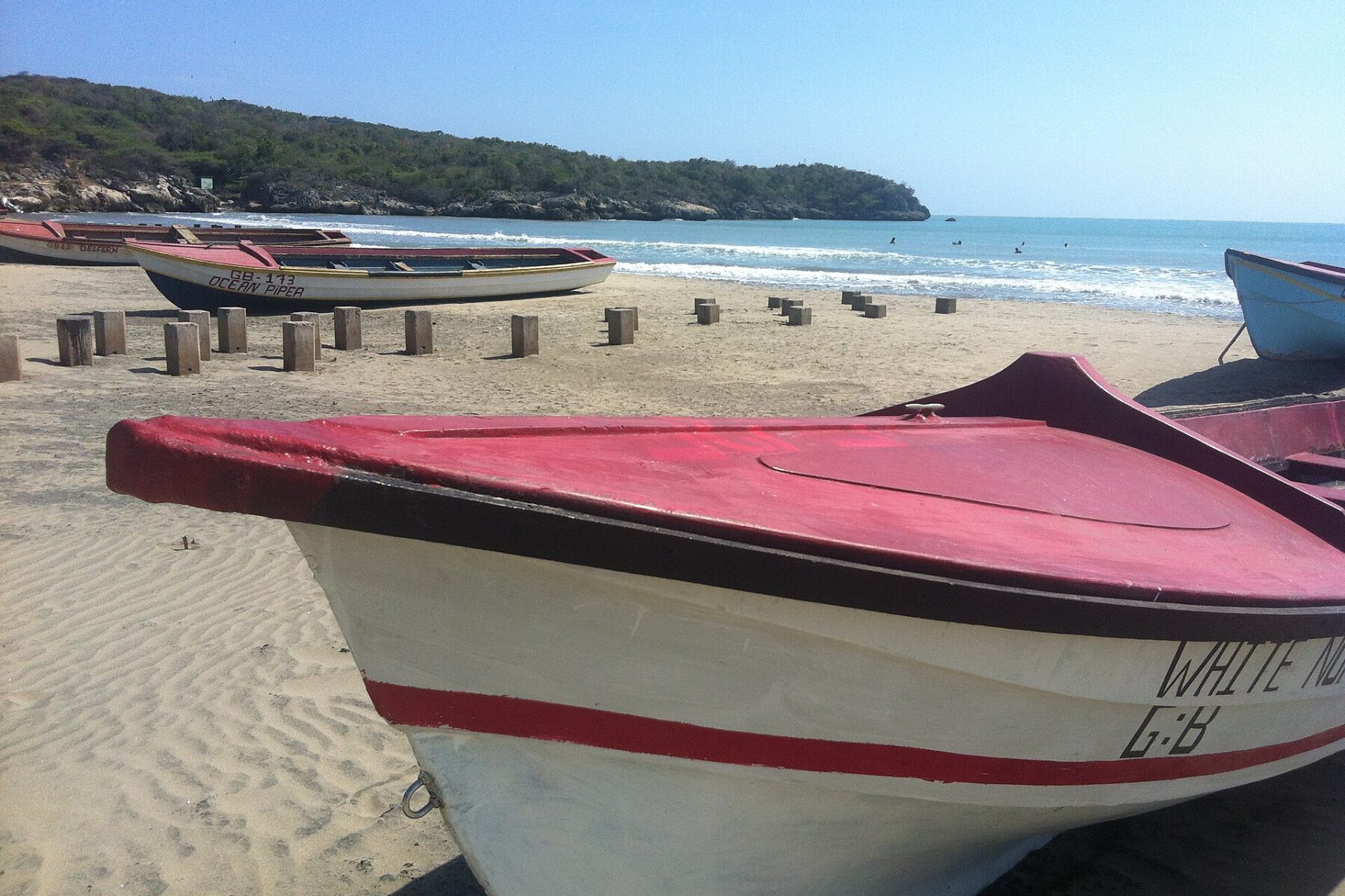 Wooden fishing boats pulled up on a sandy beach at Treasure Beach on Jamaica's south coast, with a wooded headland and blue sea behind