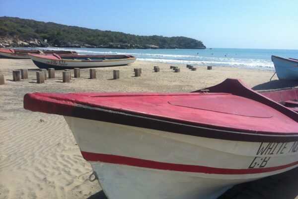 Wooden fishing boats pulled up on a sandy beach at Treasure Beach on Jamaica's south coast, with a wooded headland and blue sea behind