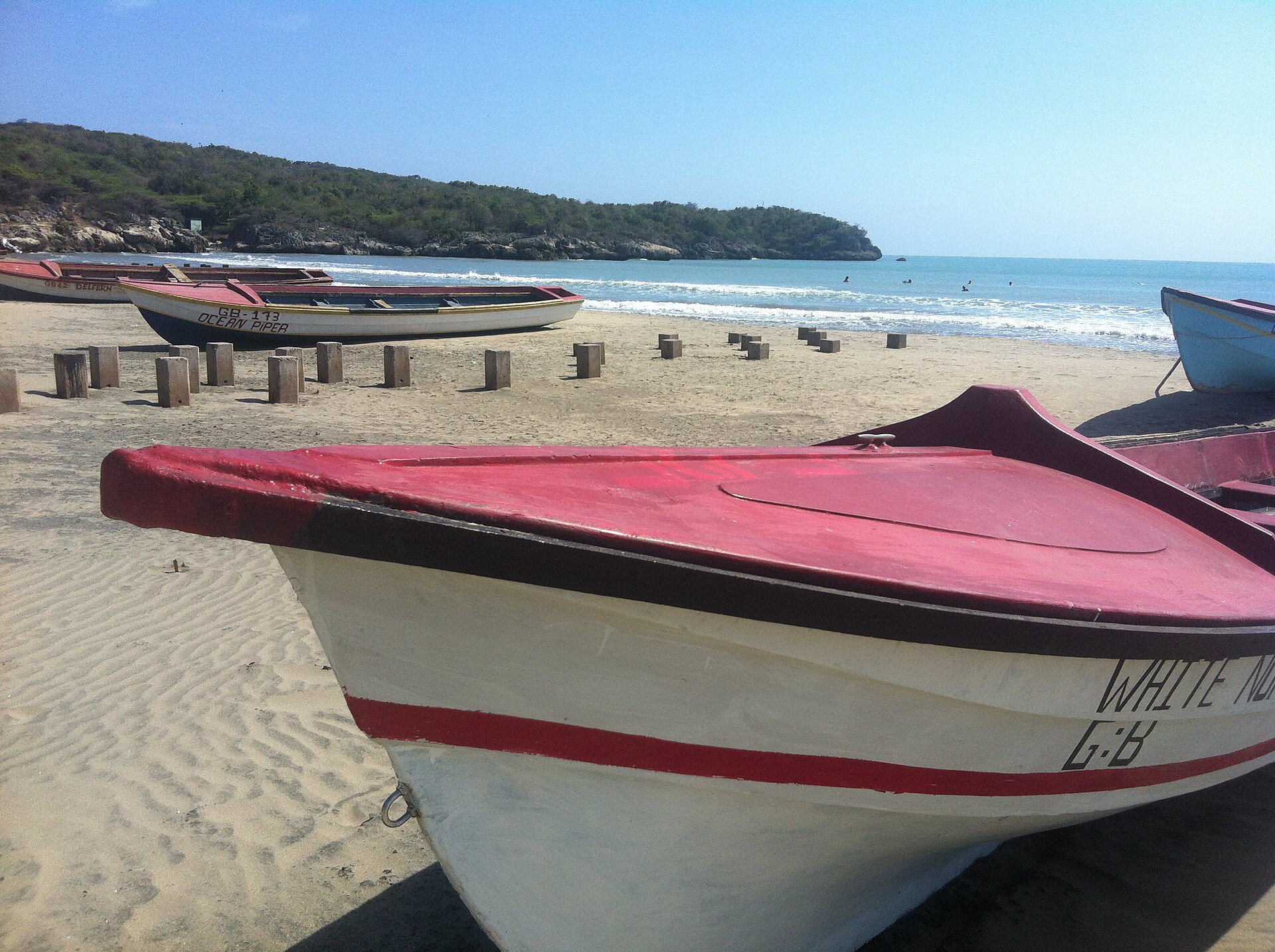 Wooden fishing boats pulled up on a sandy beach at Treasure Beach on Jamaica's south coast, with a wooded headland and blue sea behind