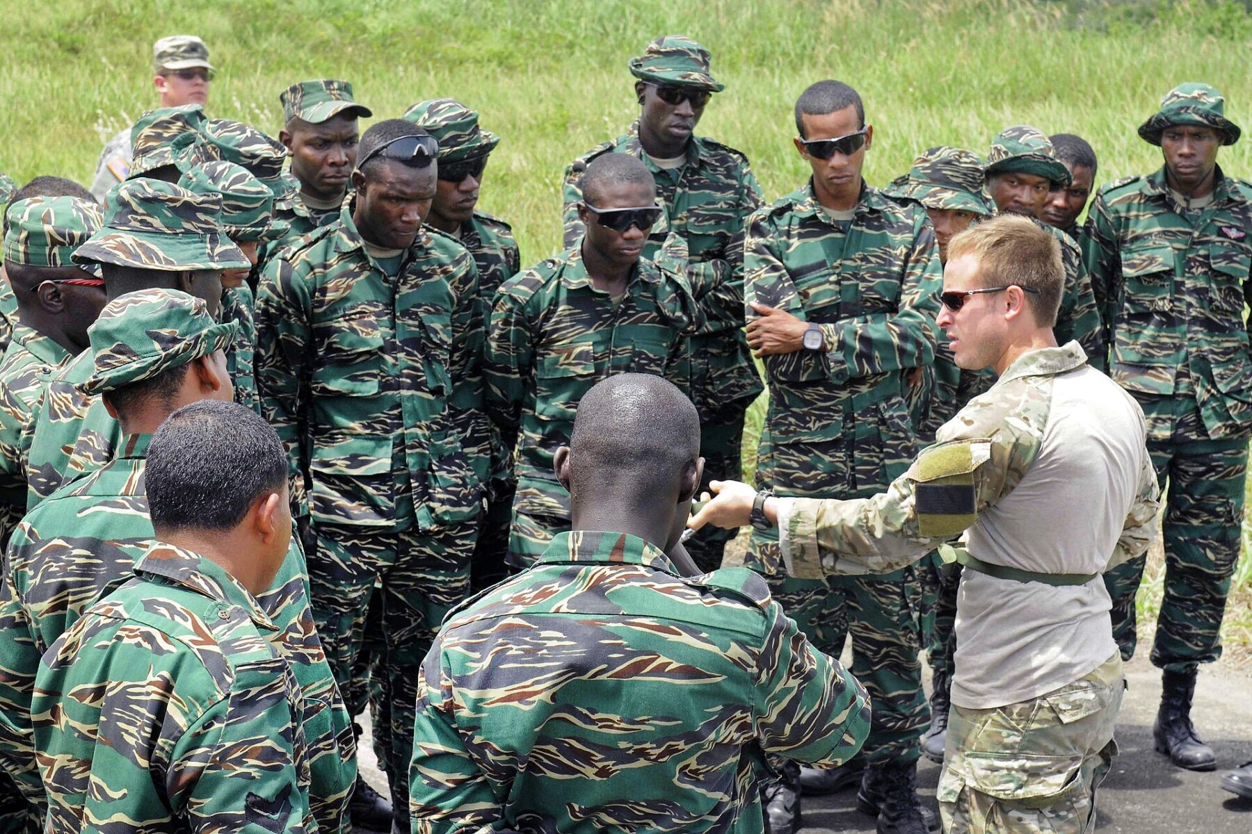 Guyana Defence Force soldiers in camouflage gather around a US special operations instructor who is explaining a technique outdoors