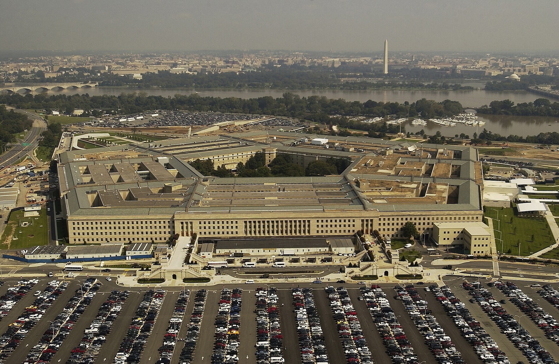 Aerial view of the five-sided Pentagon building and its parking lots, with the Potomac River and Washington Monument behind
