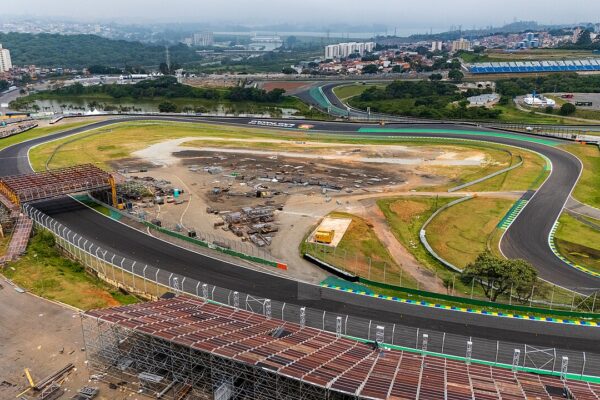 Aerial view of the Interlagos motor-racing circuit in São Paulo, with a curved asphalt track, grass infield, temporary stands in the foreground and apartment blocks beyond.