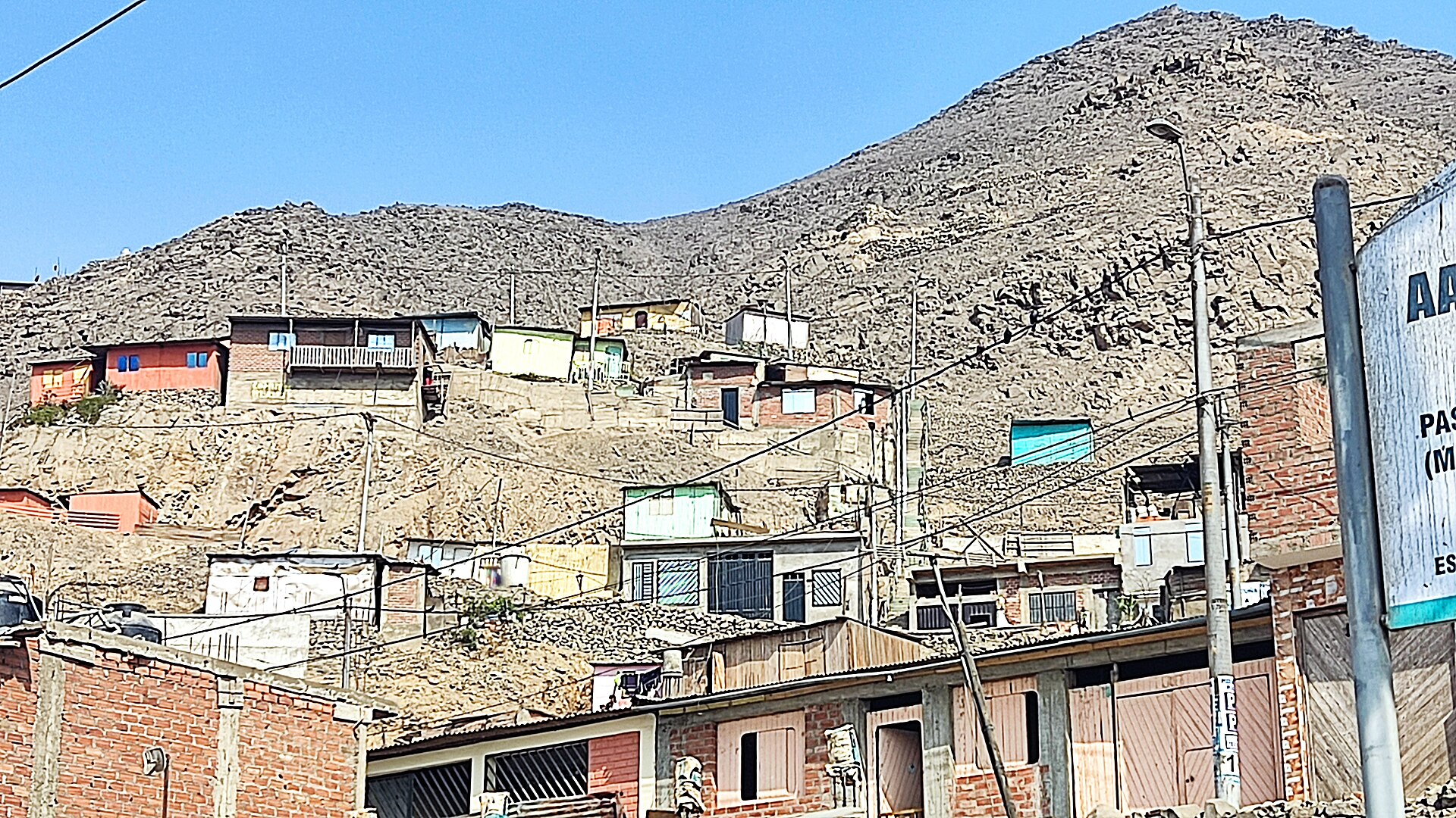 Brick and wooden houses climbing a dry, rocky hillside in Carabayllo under a blue sky