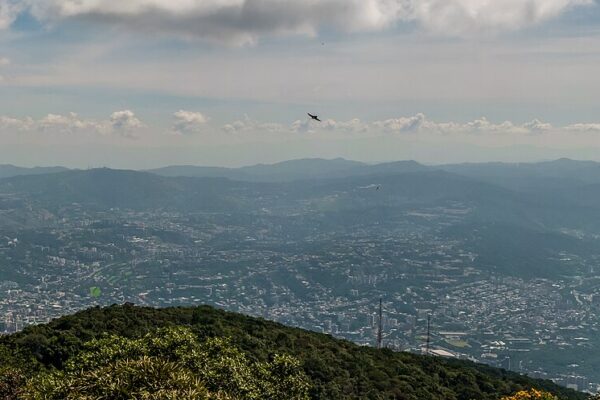 A wide view across the Caracas valley and its sprawling city from the green slopes of El Avila mountain under a partly cloudy sky