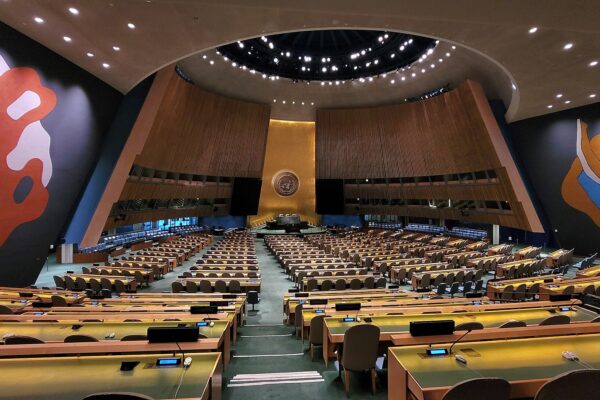 Empty United Nations General Assembly hall with the gold UN emblem on the podium wall and two large abstract murals on either side