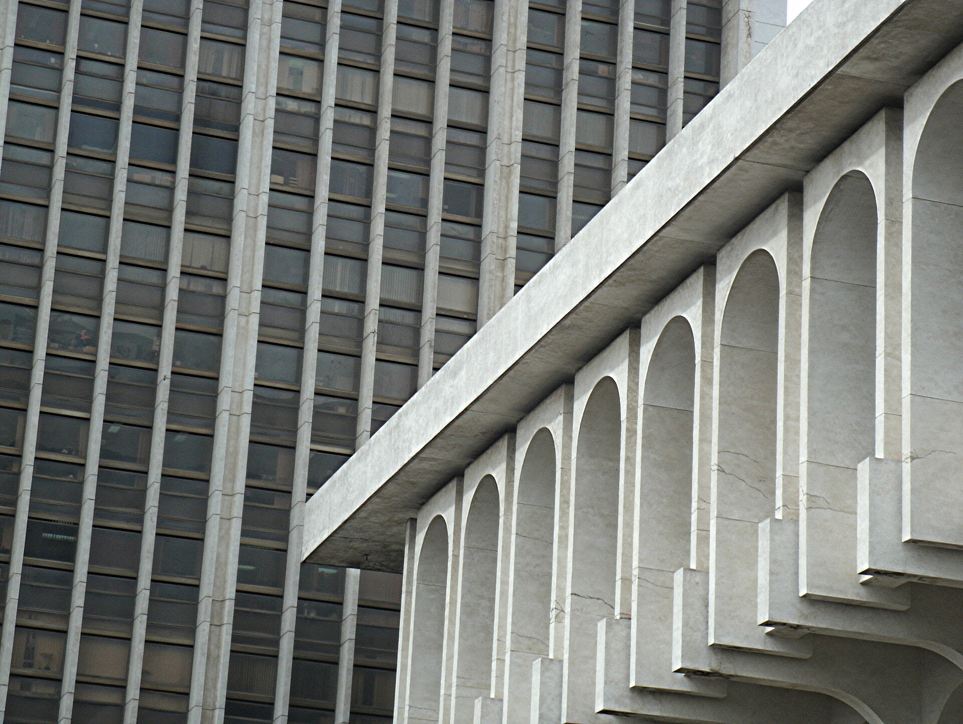 Close-up of a grey high-rise with vertical concrete fins beside a white building with a row of arches