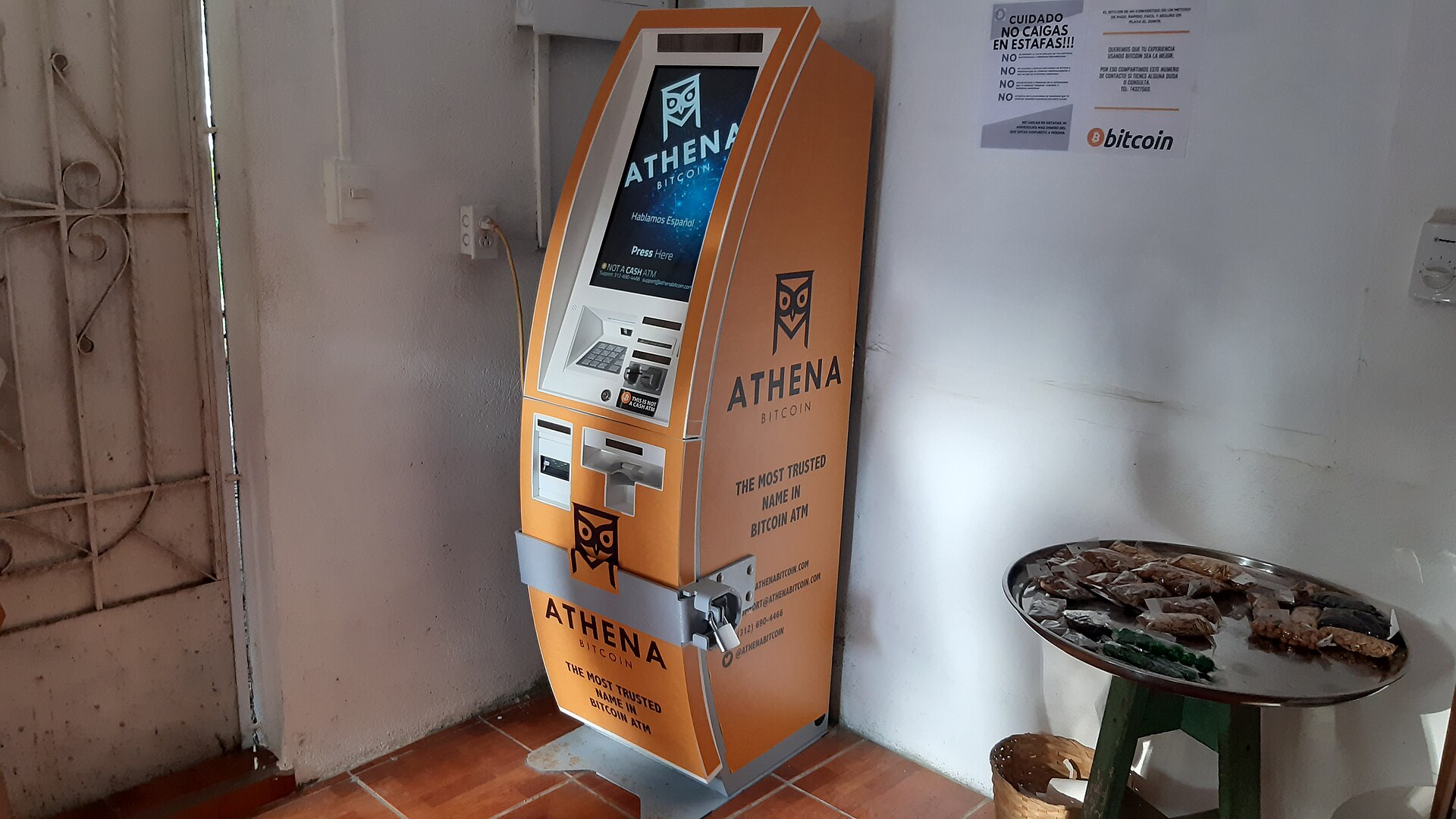 An orange Bitcoin cash machine with a screen and keypad standing against a white wall on a tiled floor in El Zonte, El Salvador