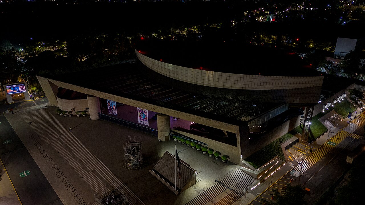 Night-time aerial view of the Auditorio Nacional in Mexico City, with its lit forecourt and concert posters on the facade