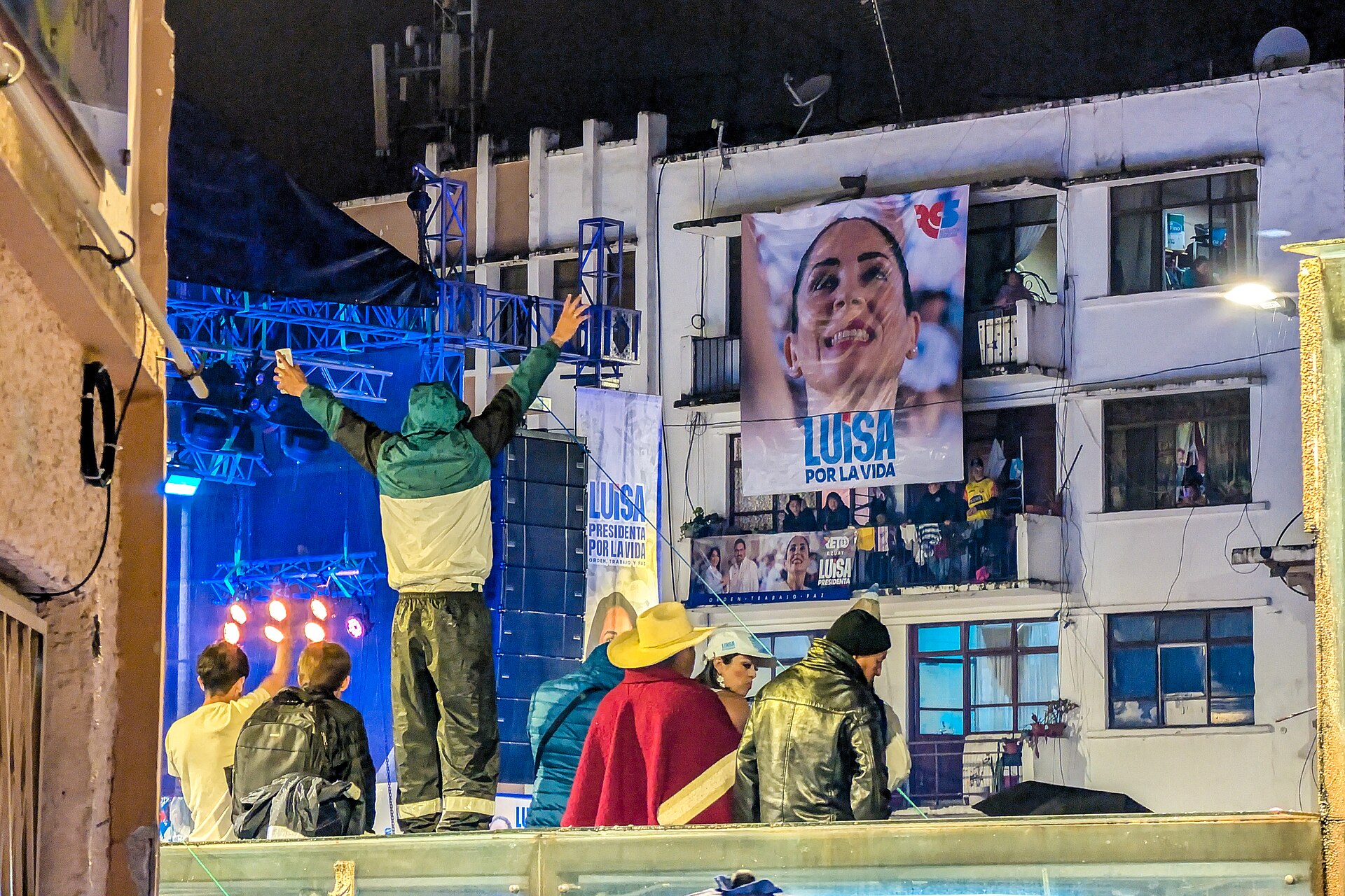 Luisa González campaign rally banner and crowd at a night event in Cuenca, Ecuador