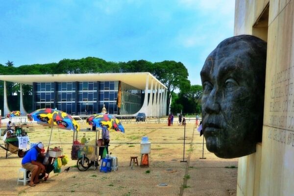 Street vendors under colourful umbrellas on the Praça dos Três Poderes in Brasília, with the Supreme Federal Court building and a bronze head sculpture