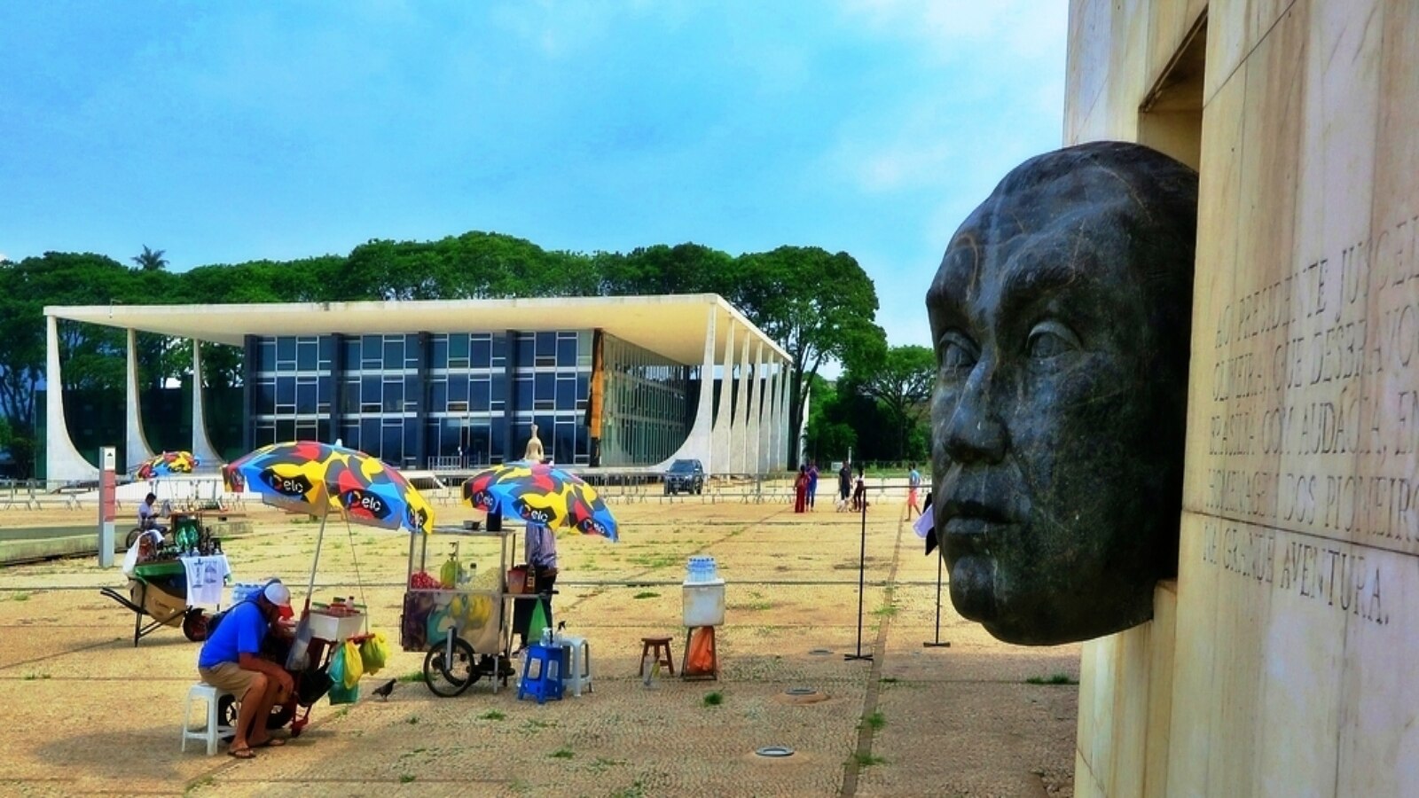 A street vendor under colorful umbrellas on the Praça dos Três Poderes in Brasilia, with the Supreme Federal Court building behind