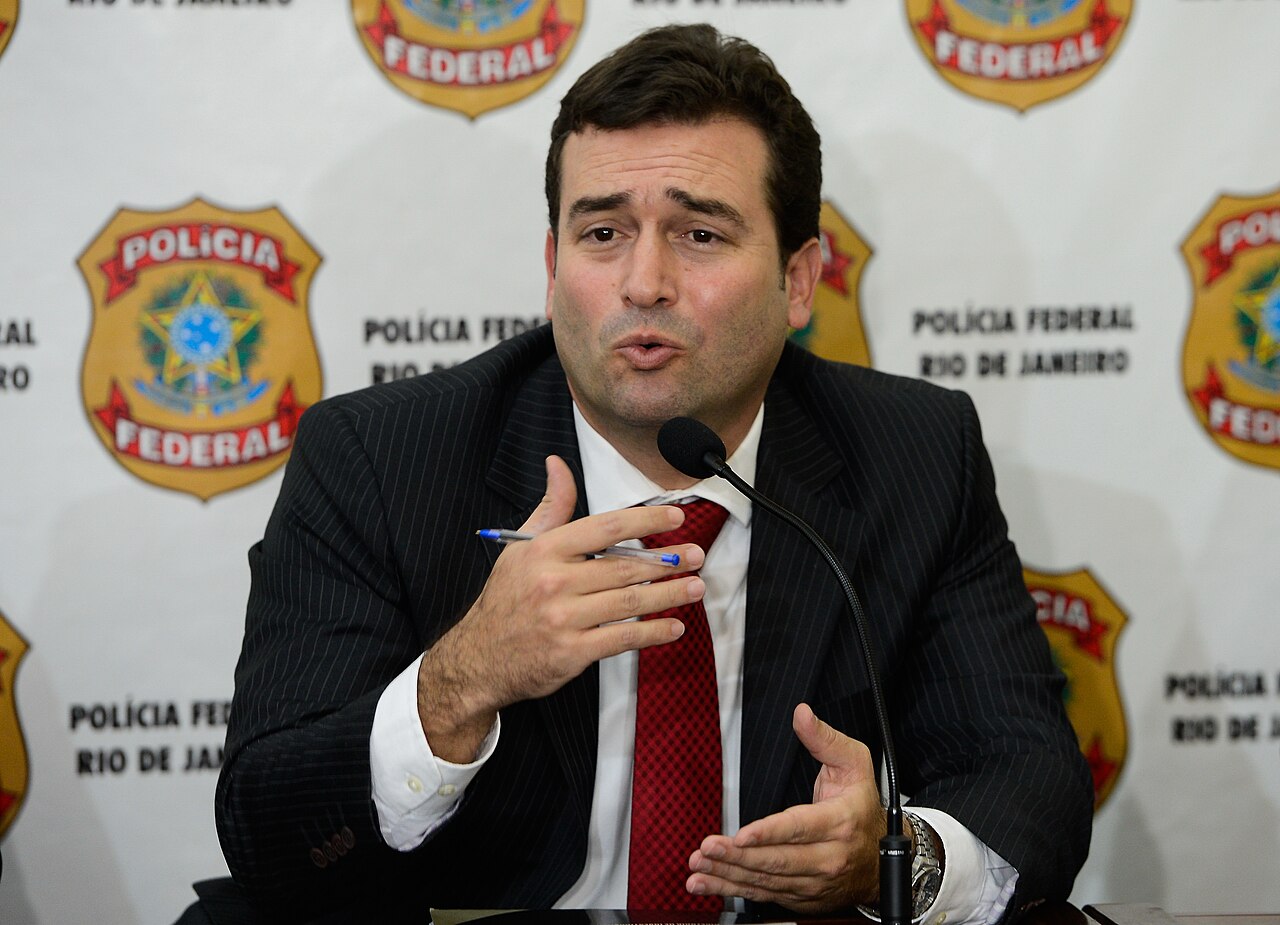 A Federal Police officer speaks into a microphone in front of a backdrop of Polícia Federal badges in Rio de Janeiro