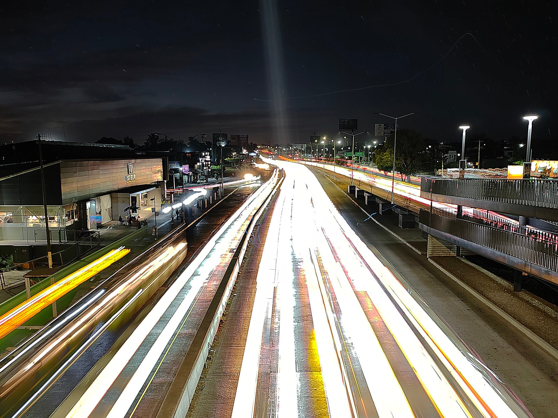 Long-exposure night photo of Periférico Norte in Zapopan, Jalisco, with streaks of car lights beside a bus rapid transit station