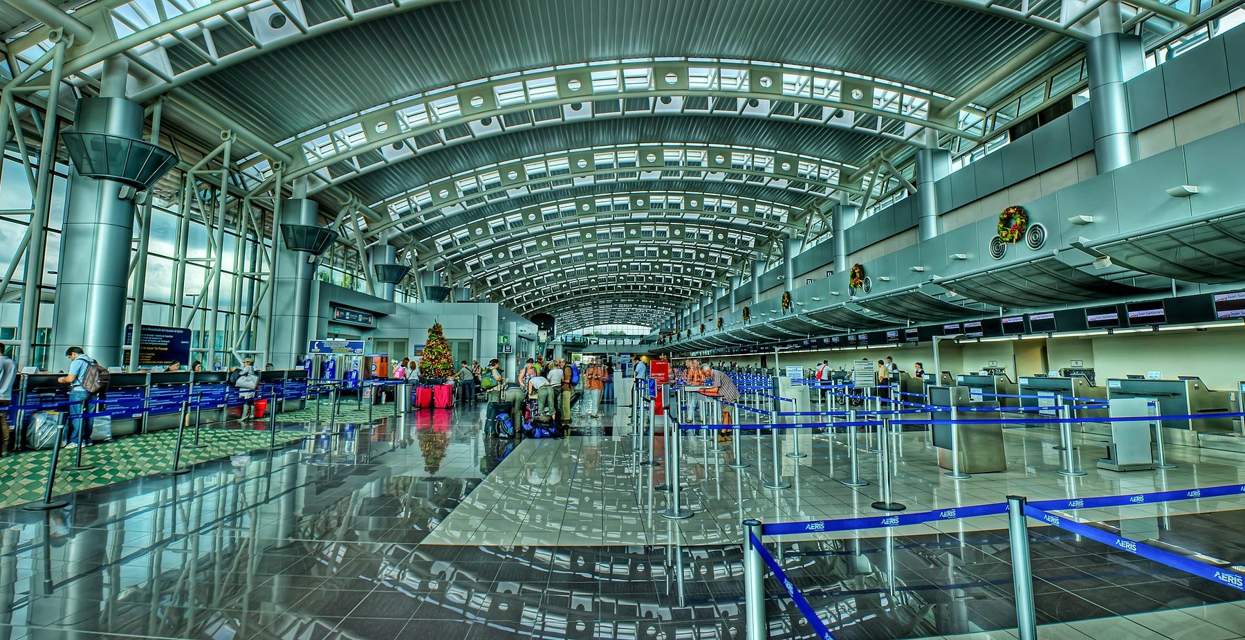 Wide hall of the Juan Santamaría International Airport near San José with check-in desks, queue barriers and a vaulted glass roof