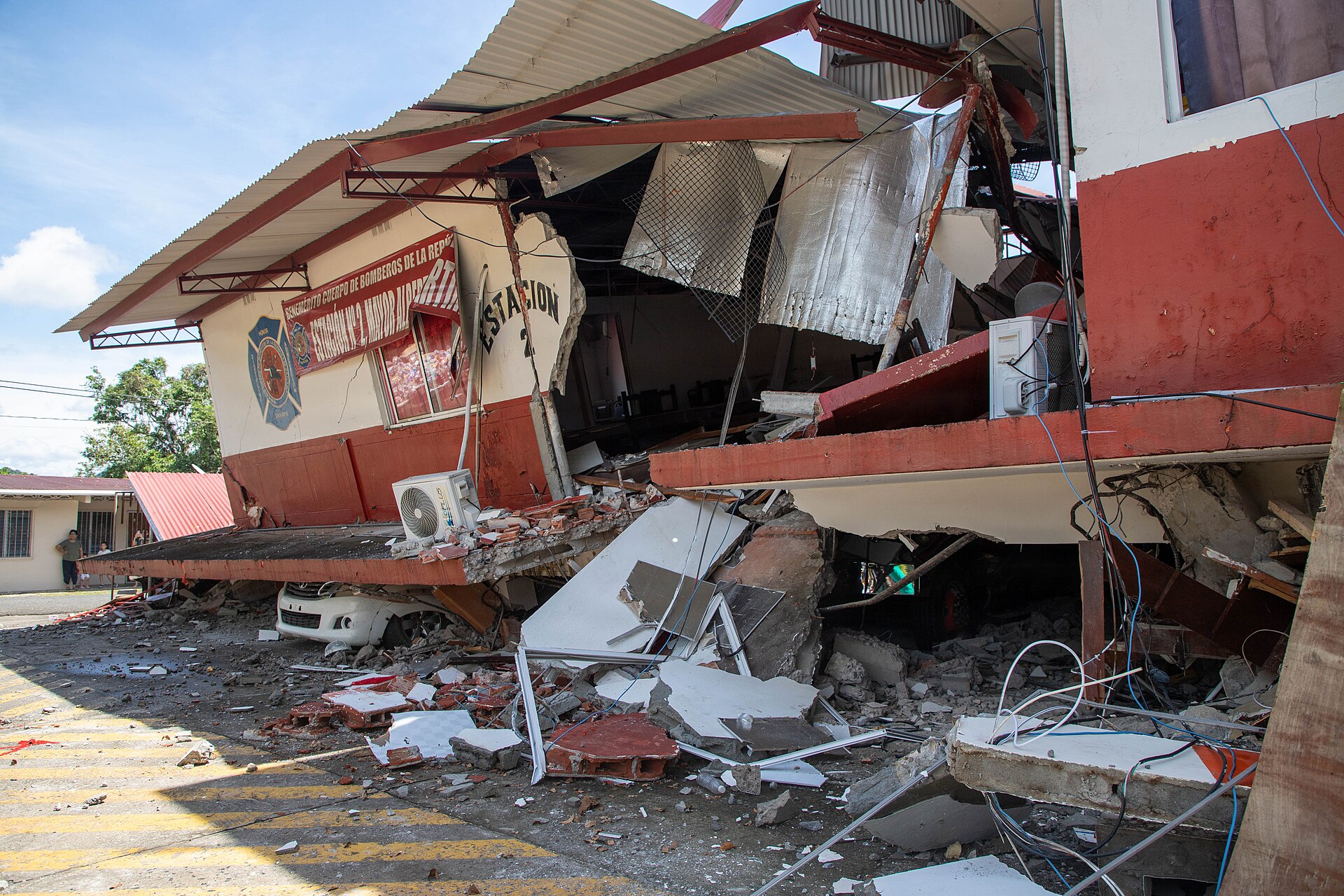 The front of a fire station of Panama's fire service torn open by the earthquake, with rubble, bent metal and a crushed white car beneath the fallen upper floor