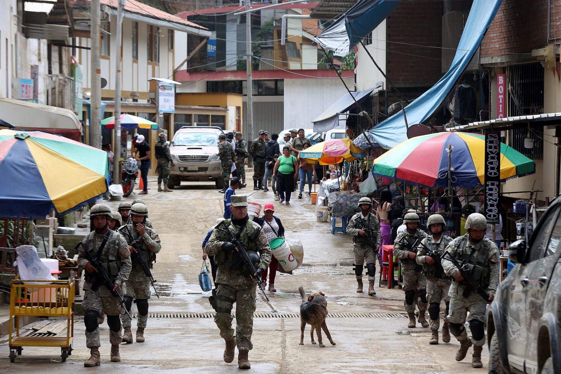 Peruvian soldiers in helmets and body armour patrol a market street lined with colourful umbrellas in Pataz