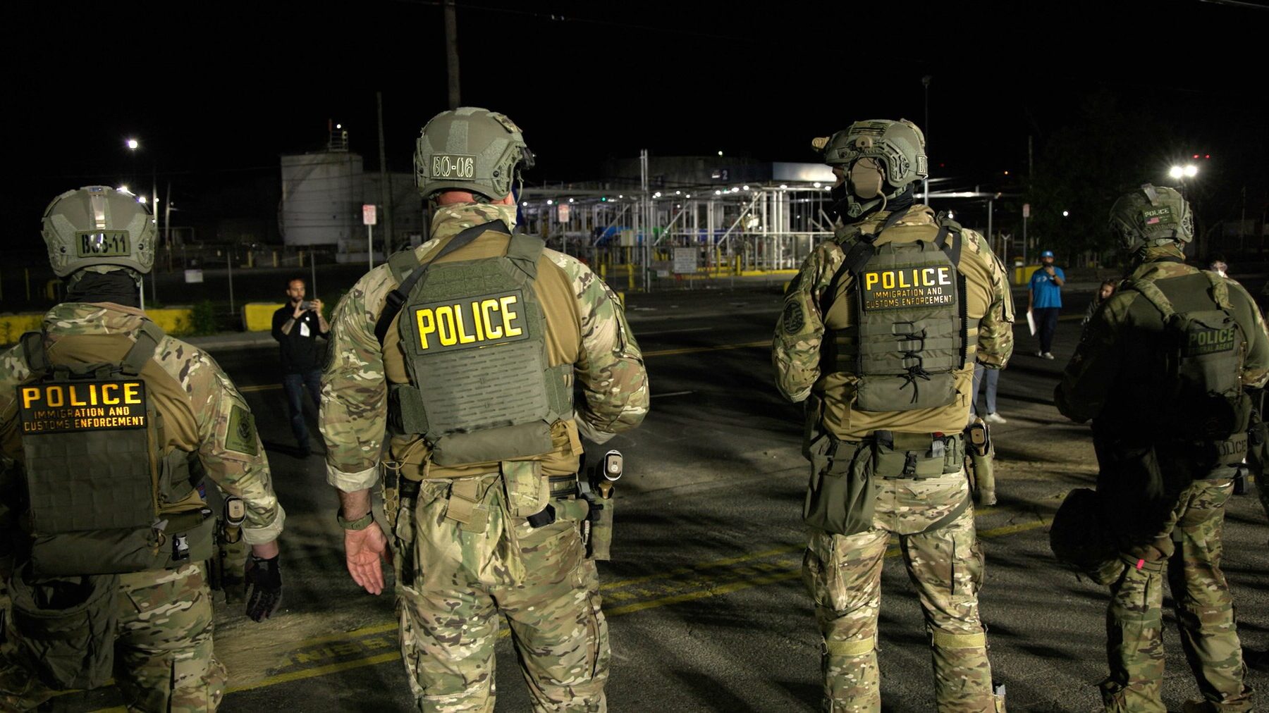 Officers in camouflage and ICE police vests stand at night on the road outside Delaney Hall in Newark, New Jersey