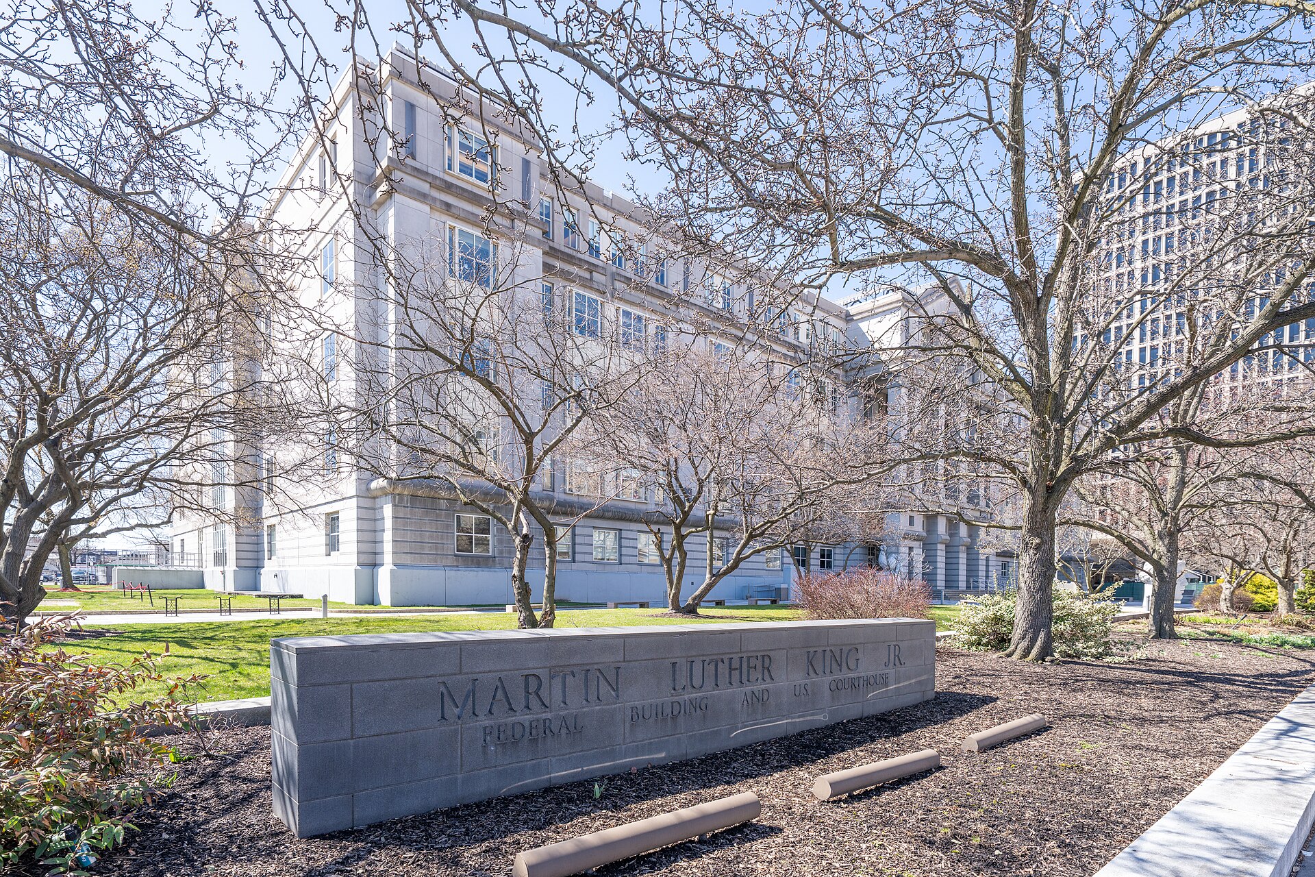 Stone sign reading Martin Luther King Jr. Federal Building and US Courthouse in front of a pale stone government building and bare trees in Newark