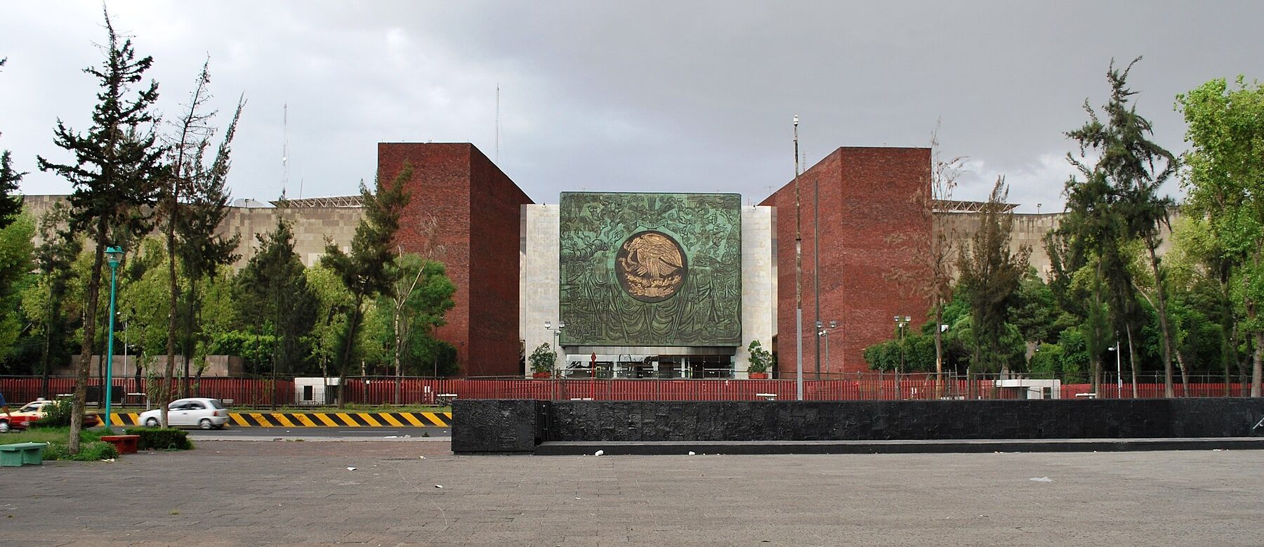 Main facade of the Legislative Palace of San Lázaro in Mexico City, with a green relief of the national coat of arms above the entrance and trees in front