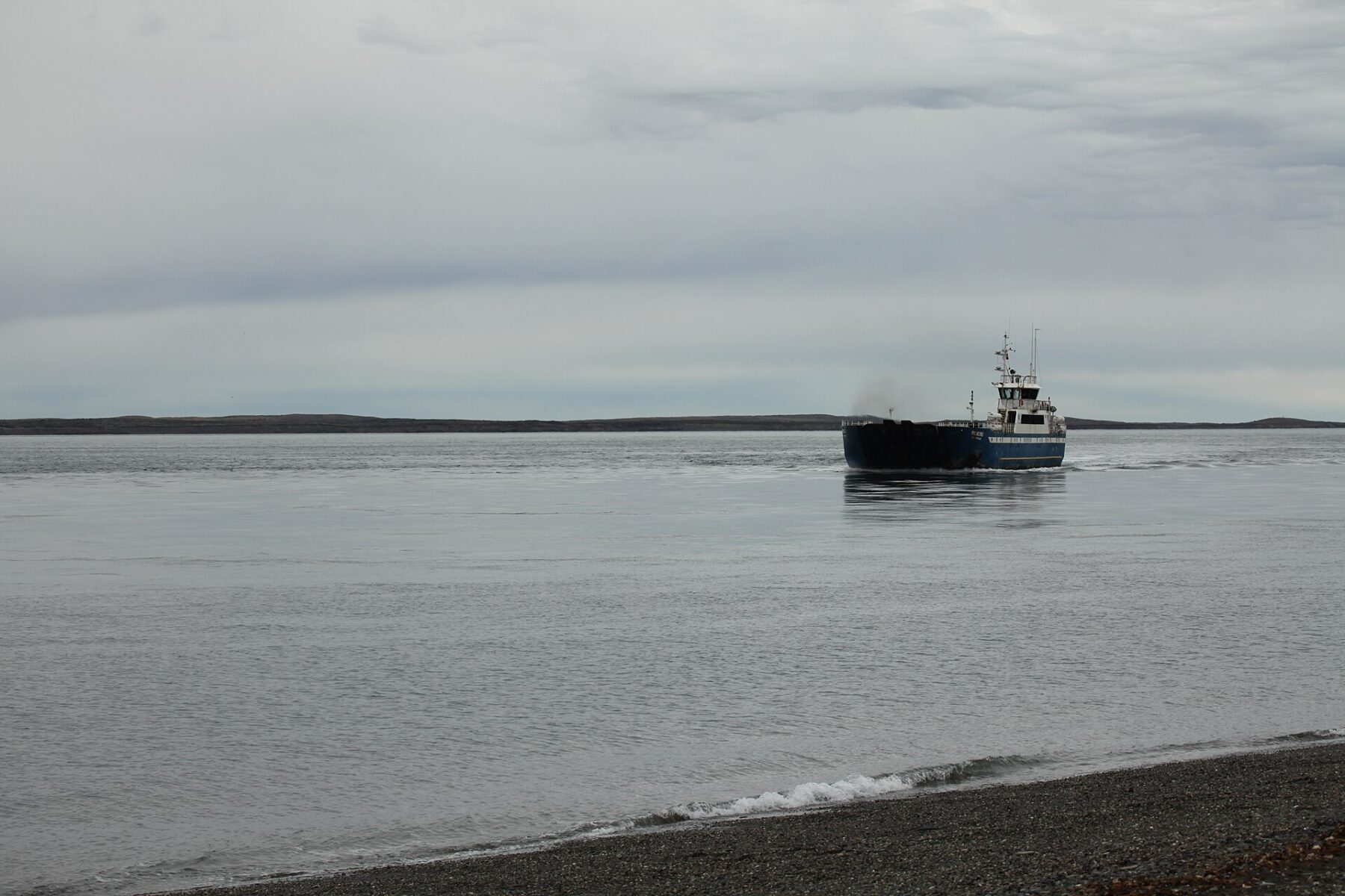 A ferry crossing the grey waters of the Strait of Magellan with a low coastline behind it