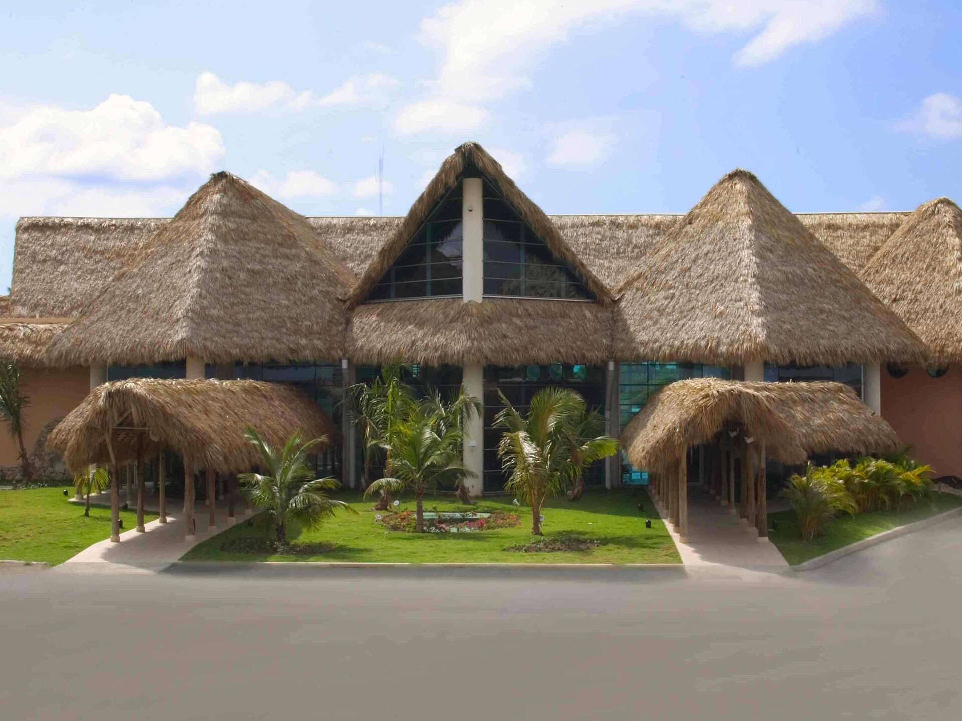 Thatched-roof terminal building of Punta Cana International Airport with palm trees and a lawn in front