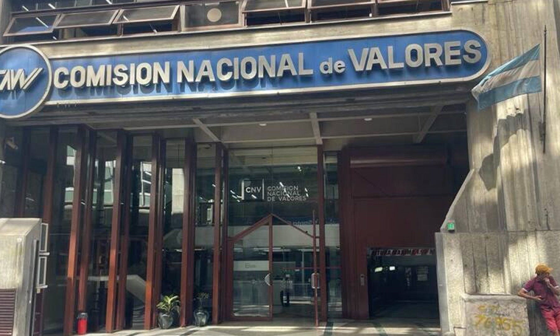 Entrance of the Comisión Nacional de Valores headquarters in Buenos Aires, with its blue sign, glass doors and an Argentine flag