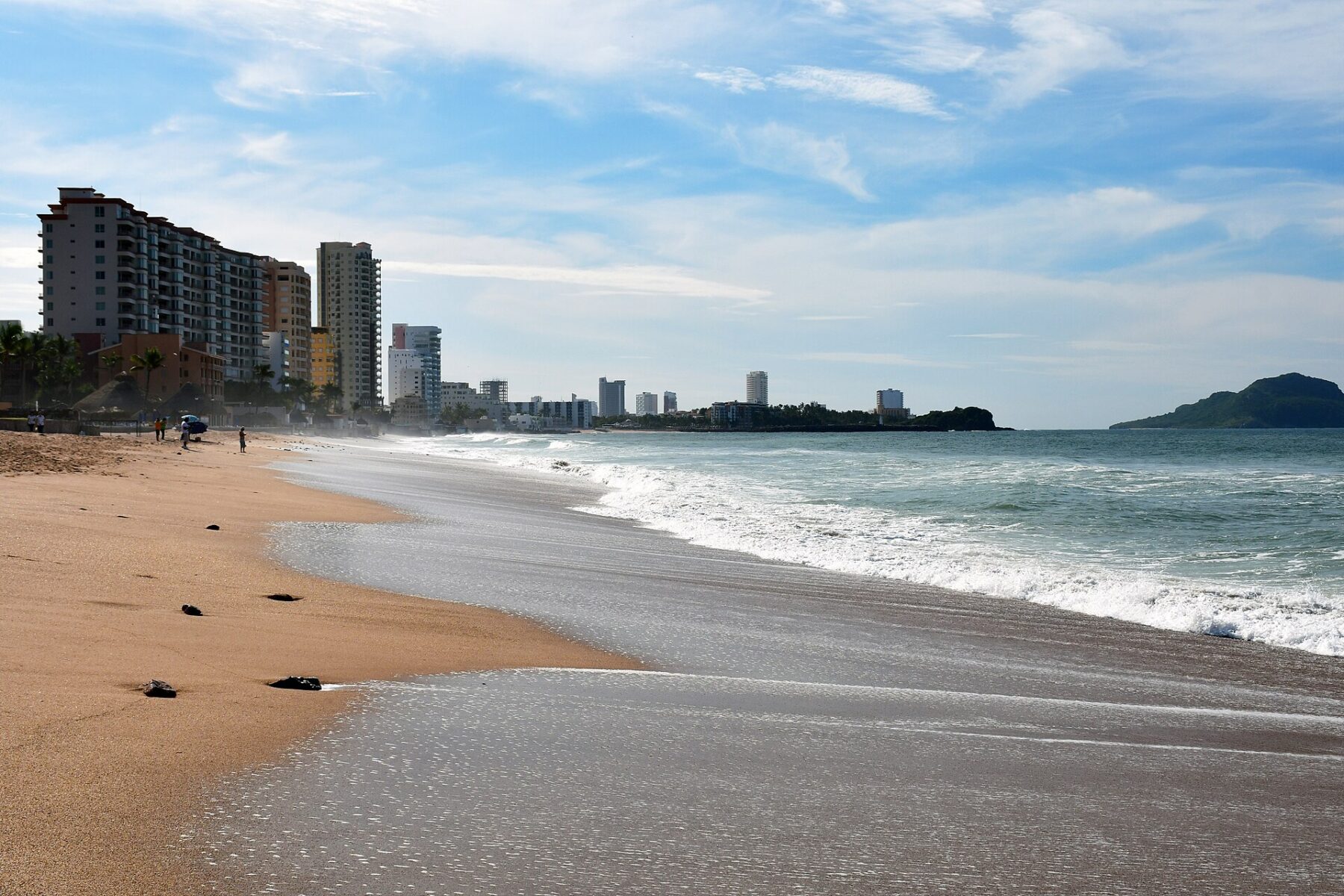 A sandy beach with waves running up the shore and a row of hotel and apartment towers along the coast in Mazatlán's Zona Dorada