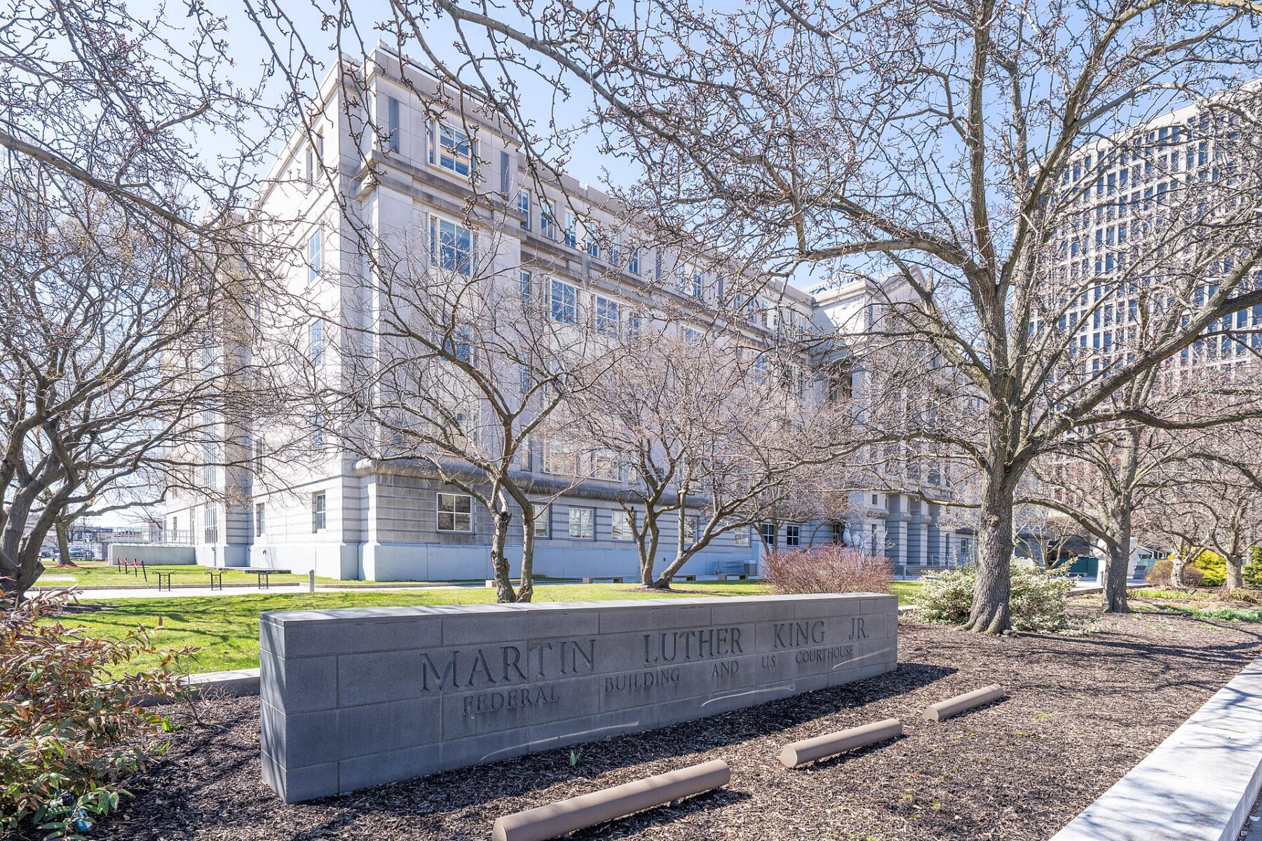A stone sign reading Martin Luther King Jr Federal Building and US Courthouse in front of a pale stone federal building and bare trees in Newark