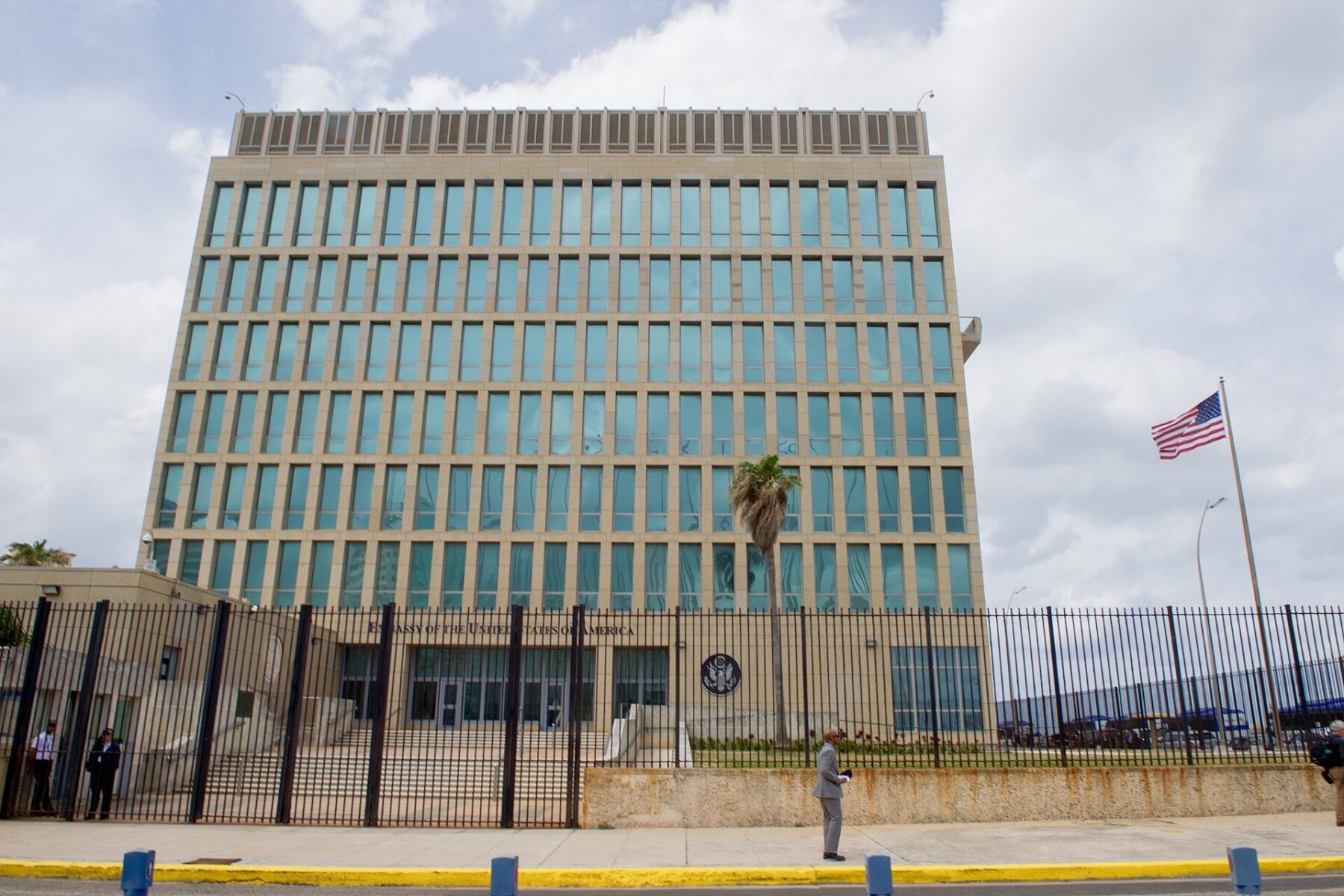The US Embassy building in Havana behind a black iron fence, with the US flag flying on a pole to the right