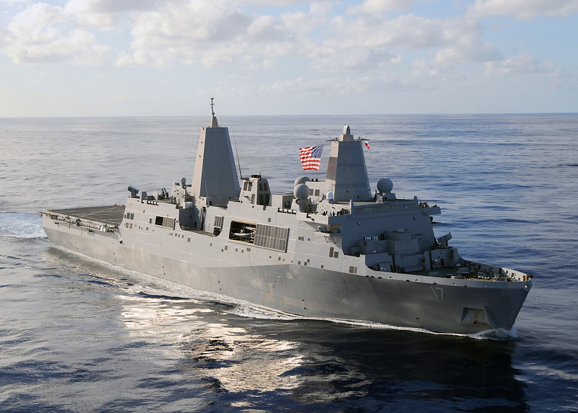 The grey US Navy amphibious transport dock ship USS San Antonio under way on open sea with a US flag flying from its mast