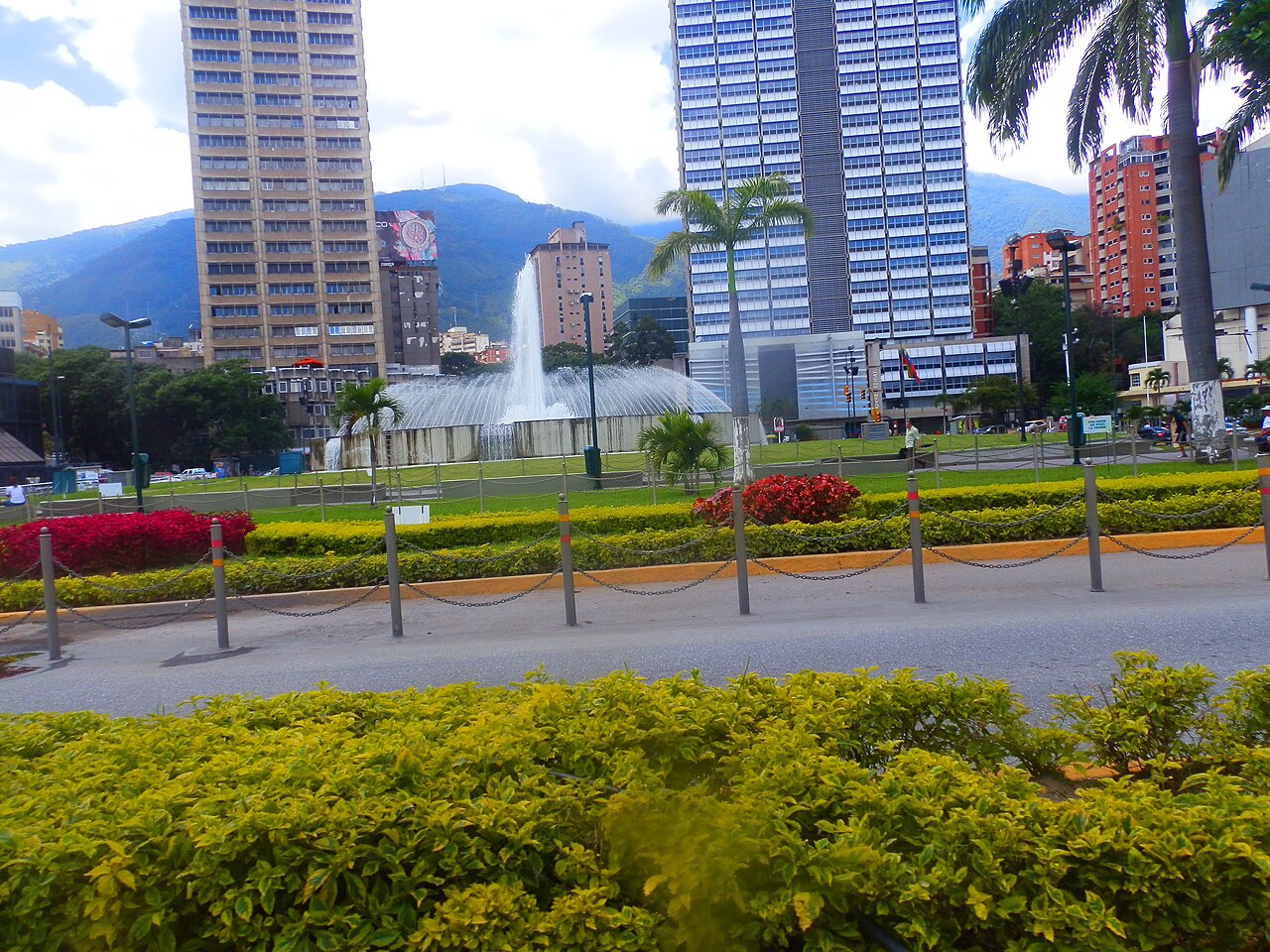A fountain and office towers at Plaza Venezuela in Caracas with green hills behind