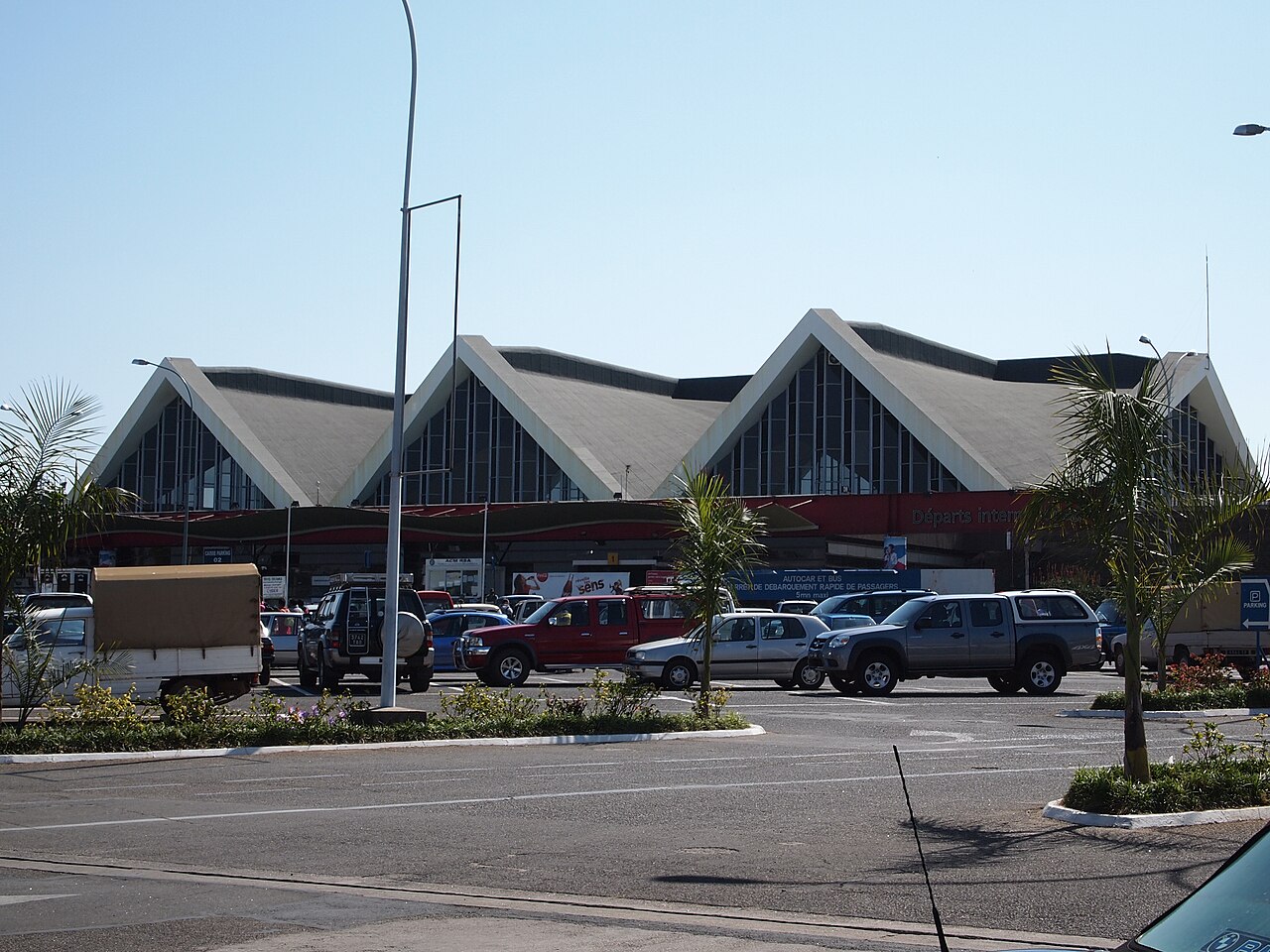Three-gabled departures hall of Ivato international airport in Antananarivo with cars and palm trees in front